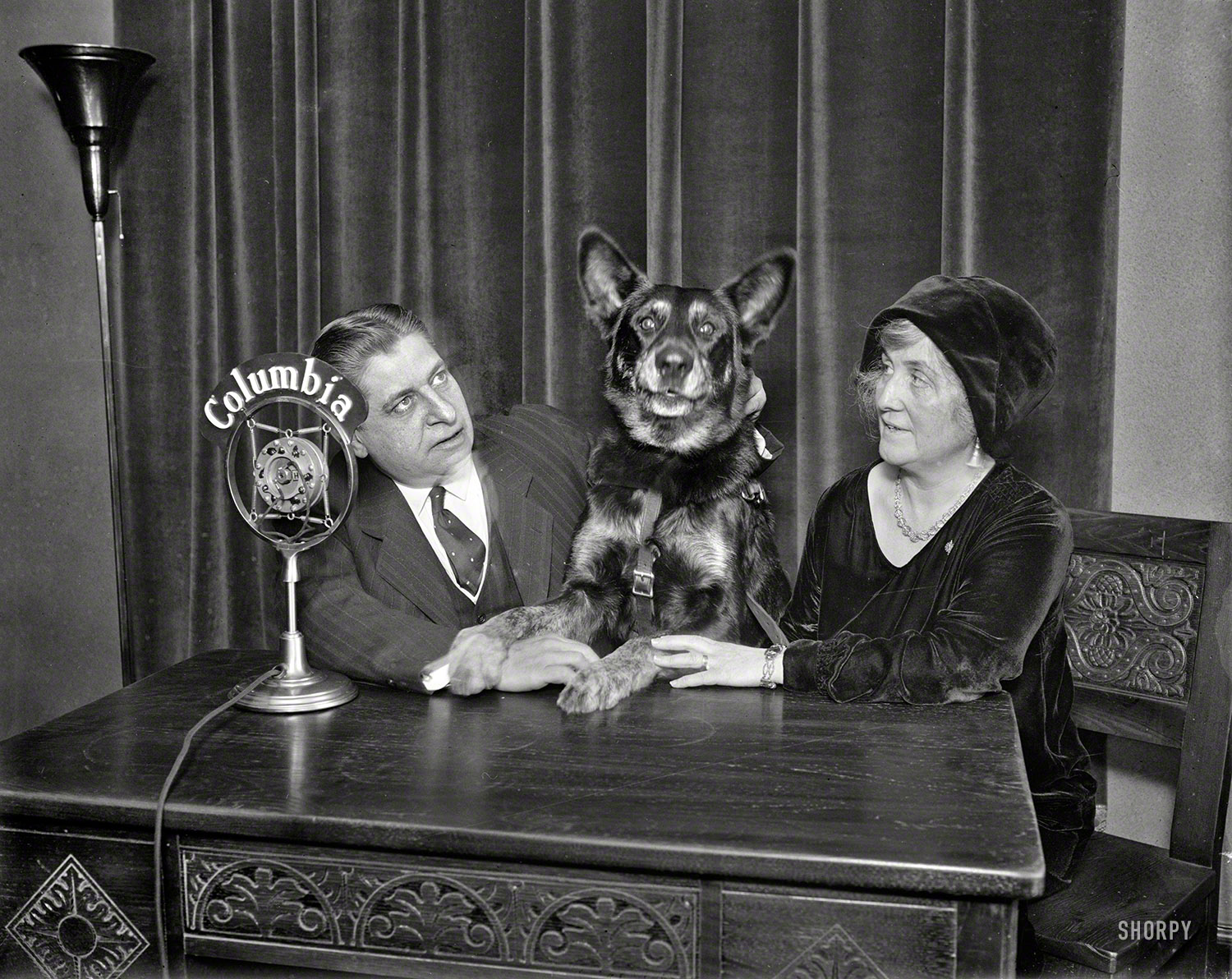 UPDATE: The photo now has a caption.

January or February 1930. Thomas David Schall with dog and woman at Columbia microphone.

Circa 1930 Washington, D.C. Not only can Fido sit, stay and speak, he (or she) can also broadcast. Unlabeled Harris & Ewing glass plate. View full size.