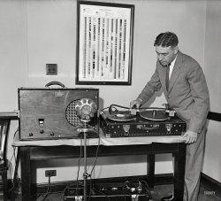 Washington, D.C., 1931. "Man with portable radio receiver and phonograph." Who seems to be using the amplifier to play a record into a microphone. Note handy "Radio Spectrum" chart. Harris &amp; Ewing glass negative. View full size.
Two turntables and a microphone This is an amazing 39 years before Beck was born 
Heavy, dude, heavy...Those cartridges and headshells look like they weigh at least 16 pounds - hope those records are made of something a little more substantial than acetate...
Spectrum chartI would love to get a close look at that spectrum chart. In 1931 40 megahertz ("megacycles" in those days) was about the limit of radio technology. Today I have a spectrum chart on my wall that goes to 150 gigahertz. That's 150,000 megahertz.
Electrical TranscriptionActually, what is happening here is the production of an electrical transcription. The disk isn't being played into the microphone--it's going the other direction. The radio broadcast is being recorded onto the disks for playback later or for archival purposes.
When I worked in radio in the early eighties, there was still a check box on the daily log to indicate that the audio source was "ET." I suspect things have caught up by now.
[The turntable is an RCA Photophone similar to the "Theatre Phonograph" in the illustration below. These were used to play background music during seating and intermission in the early days of sound pictures. They could also be used to pipe radio into the cinema. - Dave]
Victor Home Recording BlankFrom the label I can identify the record as a Victor Home Recording blank. The plastic records were pre-grooved, so the recording process was done by embossing, not cutting. It's a little harder to judge, but from the photo it looks like the grooves are already modulated, so we're seeing the record being played back.
Surprisingly lightI have a working 1933 RCA Victor combination radio phonograph with a very similar tone arm and thumb screw needle. I don't know if it's made of aluminum or pot metal, but it doesn't weigh nearly as much as it looks as though it would. I wouldn't try it on a 1950s or newer plastic record, but it does well playing both the pre-war shellack and Durium cardboard Hit Of The Week 78s of that era.
Federal Radio Commission recorderThis description is from a news photo in 1931: 
A new type of portable radio recorder has been invented. The apparatus is a portable disc equipment consisting of two motor-driven turntables, a recording amplifier, a nmicrophone, radio receiver and a loudspeaker. Pre-grooved blank disc records are placed upon each of the turntables, and when in operation, with sound being recorded as it emanates from a loudspeaker, the records operate continuously and automatically change from one to the other. This device is expected to help the Federal Radio Commission in settling any problems of programs on the air, having had to use stenographic reports until now.
(Technology, The Gallery, D.C., Harris + Ewing)