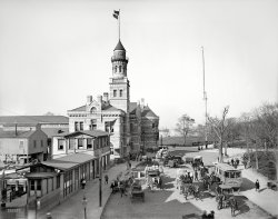 Circa 1900. "Barge Office, New York." Meet you at the Lunch Wagon. 8x10 inch dry plate glass negative, Detroit Photographic Company. View full size.
Food trucksGuess the "craze" is nothing new!
Although one wonders where along the Roach Coach-to-Gourmet Foodie Truck continuum the Lunch Wagons lie.
Your ancestors may have arrived hereLocated in Battery Park at the southern tip of Manhattan, the Barge Office was built in 1883 as customs and immigration offices. It also held offices for the Marine Hospital Service, the predecessor of the U.S. Public Health Service. It would be forgotten today except that on two occasions it served as the main processing center for people immigrating to the United States.  Its first tenure as such began in April 1890 following the closure of the nearby Castle Clinton processing center, and lasted until the end of 1891, when a huge modern facility opened on Ellis Island.  Castle Clinton had to be closed while Ellis Island was still under construction because the federal government's lease from the State of New York had expired.  
In June 1897, a disgruntled night watchman set fire to the Ellis Island facility, causing so much damage that the Barge Office had to be pressed into service yet again for processing immigrants. It served this function until Ellis Island reopened in December 1900. The Barge Office then slipped back into obscurity as a government office building, until it was demolished in 1911.
Beasts of burdenOne must pity the team of horses near the back, warming under White Star Line blankets, that will soon be called on to pull the mountain of trunks, baskets, and bundles teetering ominously atop one of the wagons.  Lets hope for the horses sake that the passengers who were well-off enough to own such belongings do not have far to go.
In 1898, when the number of Italian immigrants to the U.S. was about half of the number in the year of this photo,  the Times would say of the Barge Office site, "Outside in the park and in special rooms the Italians of New York are constantly awaiting their friends. Express wagons stand for the bundles, bags and immigrants themselves. At the meeting there is much joy. This is for the admitted. In the meantime, in the 'pens' the 'detained' wait, eat and sleep."    
For Official Use OnlyThe wagon with the tallest load appears to have the nicest blankets on its team. They are emblazoned with:
WHITESTARLINES
                 U S MAIL
That's the company that brought us the Titanic. I wonder if they kept the contract after 1912.
Customs Service FlagOf course that lower of the two flags is the Customs Service Flag consisting of 16 alternate red and white vertical stripes with a white canton bearing the US Eagle and an arc of 13 stars all in blue. Some conspiracy theorists maintain this is the "Civil Flag" of the US that was suppressed by Lincoln, but that is incorrect. They point to a passage in Hawthorne's "Scarlet Letter" in which the main character, who is a Customs Service Employee, notes and describes the Customs Flag and refers to it as a "civil" rather than a "military" flag, which of course is true. But that doesn't make it "the Civil Flag" of the US, a concept we never adopted. We have always had only one flag, the good old Stars and Stripes, pictured here in the top most position, as it should be.
A Page out of Equine VogueThe well dressed horse this season will have a mid calf length hem and quilting on his blanket.
It must have been really cold that day. 
....I P News Office = SHIP NEWS OFFICEI wonder what News Office is in there. Anyone knows?
"(Manhattan?) Immigration Processing News Office" maybe?
Although I seem to see the word "PRESS" on the sign left from the door, so that would make more something like "(Manhattan?) Island Press News Office."
Update:
I found a solution to my puzzle. On a picture of the U.S. Barge Office - foot of Whitehall Street, East River, by E. &amp; H.T. Anthony, we can see a similar News Office (of the New York Herald), called "SHIP NEWS OFFICE."
(The Gallery, Boats & Bridges, DPC, NYC)