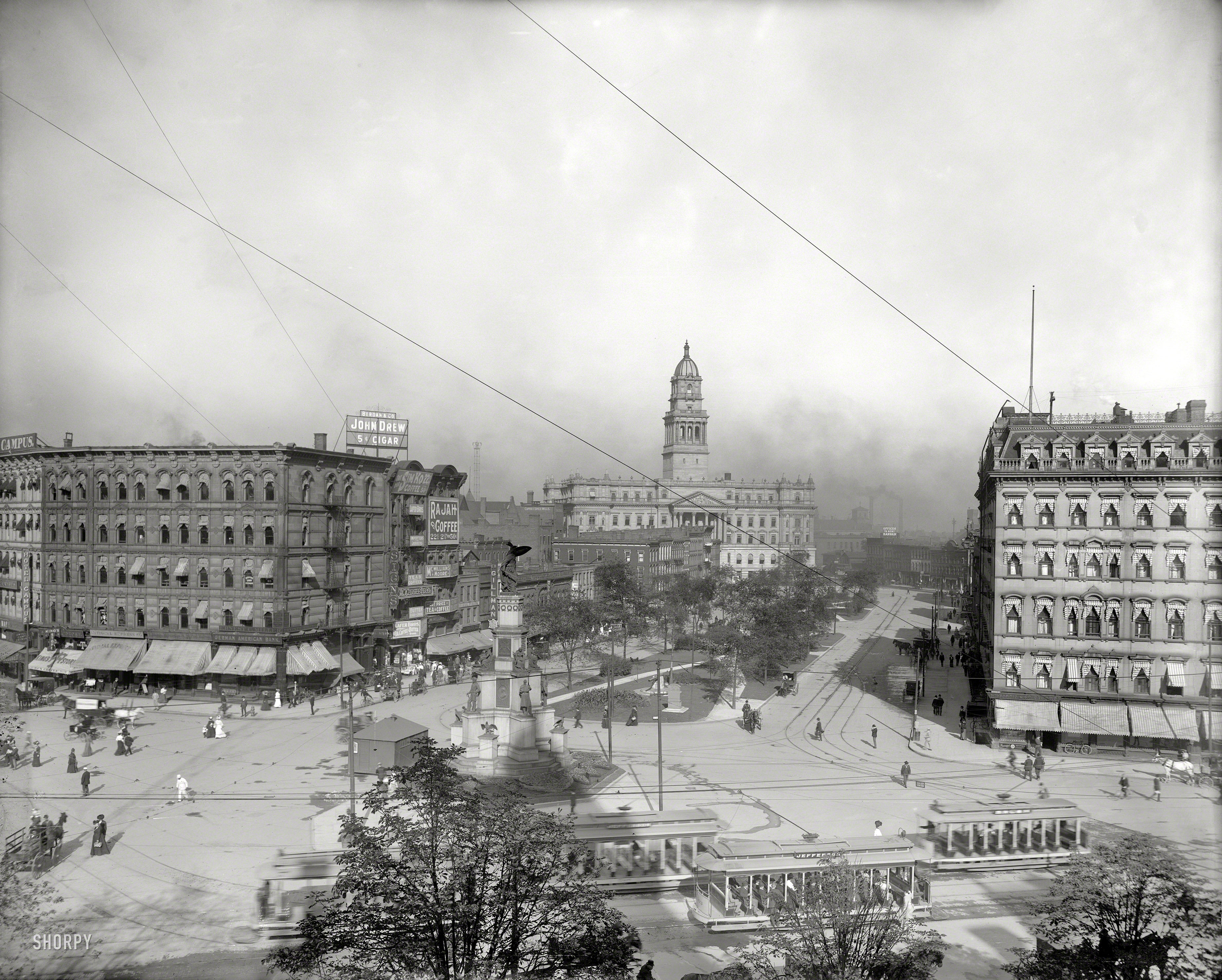 Detroit circa 1902. "Cadillac Square and Wayne County building." The rigging is for one of the "moonlight tower" arc lamps that provided nighttime illumination, an example of which can be seen behind the Rajah Coffee sign. View full size.