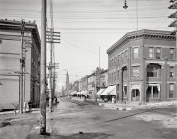 Circa 1906. "Quincy Street -- Hancock, Michigan." In the copper country of the Upper Peninsula. Detroit Publishing glass negative. View full size.
Two levels of bankingIf I am reading the signs correctly, it's First National Bank on the main floor, plus Northern Michigan Building &amp; Loan Association on the second floor. They probably weren't that competitive back then, but it's a little strange to have two financial businesses situated so closely.
Much the same107 years later, and things look much the same.  The spires and awnings are gone, and there are fewer wires criss-crossing the sky, but most of the buildings are still more or less intact.
View Larger Map
Does that place have a bank dick?A little before WC Fields.  However, if the bank on the right side of the street was robbed about that time, I think we can put the finger on the guy on the left side thinking about it.
The sharply dressed fellow in the windowOn the second floor on the right under Loan Association would never have imagined that 107 years later he'd still be looking out the same window!
The gutter.Check out the new gutters on the sidewalk. I think that is the most impressive thing in this picture. Not bad for 1906.
(The Gallery, DPC)