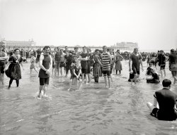 New Jersey circa 1905. "On the beach at Atlantic City." A lively group seen earlier here. 8x10 inch glass negative, Detroit Publishing Company. View full size.
Gym, tan, laundry.Gym, tan, laundry.
Family TraditionI could weep as I look at this, the life and pleasure of the young who are now all more than 110 years old.  This was my grandparents' generation. They loved to visit Atlantic City and 20 years later my father and his three older siblings would be dancing and performing on the Million Dollar Pier, which I believe is pictured here.  The stories of my father's boyhood years, summers in Atlantic City, "the playground of the world," and especially the sights and sounds of the Million Dollar Pier, are among my favorites of his. Perhaps like the people pictured here, his family would come by train from Philadelphia (well, they had to cross the river by ferry into Camden and then get the train). The family-- grandmother, uncles, mother and children, would come for the summer, while my grandfather remained in the city, working in the foundry, earning money to keep them there.
[This photo shows the Steeplechase and Steel piers. - Dave]
Shore fast lineMy grandparents would have ranged in age from toddlers to teenagers at this time.  They were more likely to have spent summer holidays in Wildwood, though one pair of grandparents rarely missed the Miss America Pageant, which originated at Atlantic City and remained there until it was moved to Las Vegas for reasons that remain a mystery to this writer.
Reading Railroad passengers from Philadelphia took the ferry to Camden's Reading Terminal for trains to Atlantic City but after 1896, Pennsylvania Railroad passengers had the choice of through trains that crossed the Delaware River at the Pennsy's Delair Bridge. Early in the Depression, the joint Pennsylvania Reading Seashore Lines railroad was formed and the Pennsy lost its monopoly on the Delair bridge. 
Those women must have been rather uncomfortable in such voluminous bathing costumes.
Anyone?I have never understood why, in these shots of Atlantic City in the early 20th century, seemingly everyone is a) in the water and b) all bunched together. Nowadays if anyone goes into the ocean, they pretty much keep their distance (unless you are related-and surely all these people weren't) Was it just considered the social thing to do then? I am truly curious.
[I'd say it's because of a) hot weather, and b) the sheer quantity of people. - tterrace]
About ten years laterMy grandfather Harry A. Fox (far right in both images) and fellow sailors from the _USS Indiana_ on the beach at Atlantic City in 1918. In the second image they are clowning with some local children.
(The Gallery, Atlantic City, DPC, Swimming)