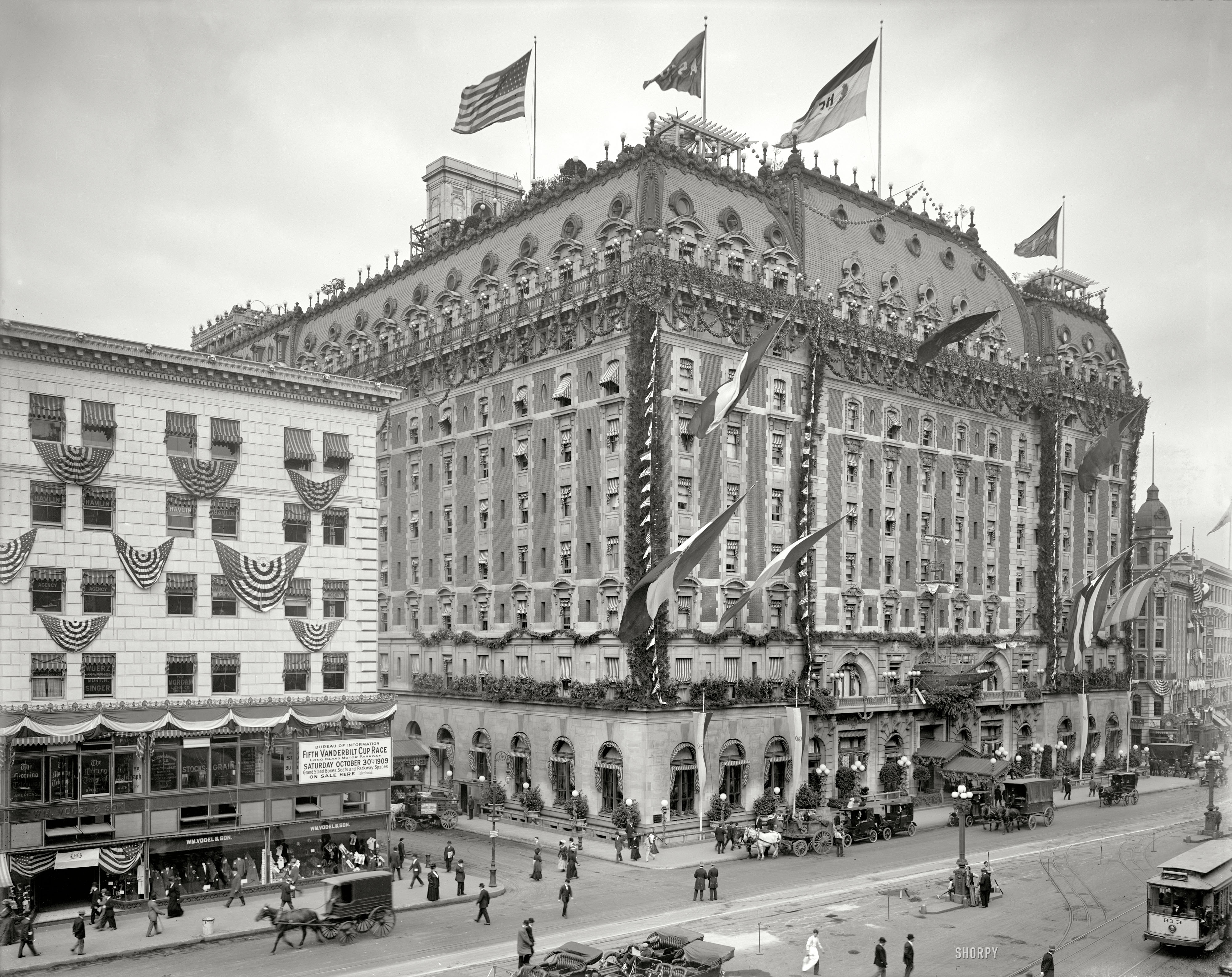 New York, 1909. "Hotel Astor, Times Square." Points of interest include the galleon lodged in the hotel facade, as well as a sign on the building next door advertising the fifth Vanderbilt Cup auto race. View full size.