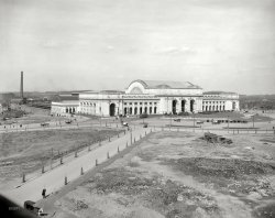 Washington, D.C., circa 1908. "New Union Station." Idyllically uncongested. 8x10 inch dry plate glass negative, Detroit Publishing Company. View full size.
Like Dulles Airport in 1964I remember it sitting in the middle of nowhere just like this. But unlike Dulles, which was built ahead of its time, Union Station was way overdue.  It was part of the "Washington Improvement" which eliminated two existing depots [including one on the Mall] and many dangerous grade crossings.
I recently found this website 
http://www.washingtonunionstation.com/about.html
which is telling the whole story of Union Station. It is the dissertation of a gentleman named Bill Wright.
I wonderif anyone heading to catch a train said, "Why'd they put it in the middle of nowhere!"
Urban renewalThe foreground dramatically illustrates how the Union Station project was used to clear out the slums north of the U.S. Capitol. Then they had to decide what to do with the cleared land: one proposal would have put the Lincoln Memorial there. Today it's a park--though actually the emphasis seems more on parkING.
Bottom leftAbove the horse. Are those two coats hanging on the poles? Probably wouldn't get away with that today.
Oh my goodness!A poor title comment but I'm kind of speechless, perhaps because I've been through this station so many times; what a difference 100 years can make.  For any who don't know, the finale of the movie Silver Streak was based on an actual crash into this station by a runaway 447,000 pound PRR locomotive pulling a passenger train.  With brakes failed, it was headed for the Great Hall when fortunately the floor collapsed and the engine ended up in the basement.  The sturdy GGI was soon back in service and no one was hurt.  Gee, I wonder if Shorpy has any photos of that 1953 event?!
Just openedI believe that this was just at the time that the station opened. First PRR train was in 1908. 
Missing PersonsJust realized that the statues on top of the columns at the front entrance had not yet been installed when this shot was taken (1974).
Still awesome! I'm a frequent user of Amtrak and have seen the best and the worst of their stations. Washington in my book is the best of the best. I always have a layover in DC on my way back to Oregon and I actually look forward to it, unlike Chicago!
Beautiful buildingInside and out. One of the highlights of my trip to DC a couple years ago was eating breakfast there. Looks so different without all the trees and surrounding buildings - and all those cabs and double-decker tour buses waiting out front.
Almost Lost ItWhat's really amazing is how close we came to losing this wonderful building.  By the early 1970's (when the building was only 60+ years old), it had become a dingy, leaking, dilapidated, rat-infested, sadly neglected dump that was very close, more than once, to being just bulldozed so we could put another dreadful soul-deadening government office building on the site, with what remained of the so-called "train station" buried under ground somewhere.  Train travel in the USA is still a shadow of what it should be (the DC-Boston corridor being one small, very modest exception), but at least we have managed to save places like this, as well as Grand Central Terminal in NY City, and South Station in Boston, along with a few scattered others.
Great photo!
(The Gallery, D.C., DPC, Railroads, Streetcars)