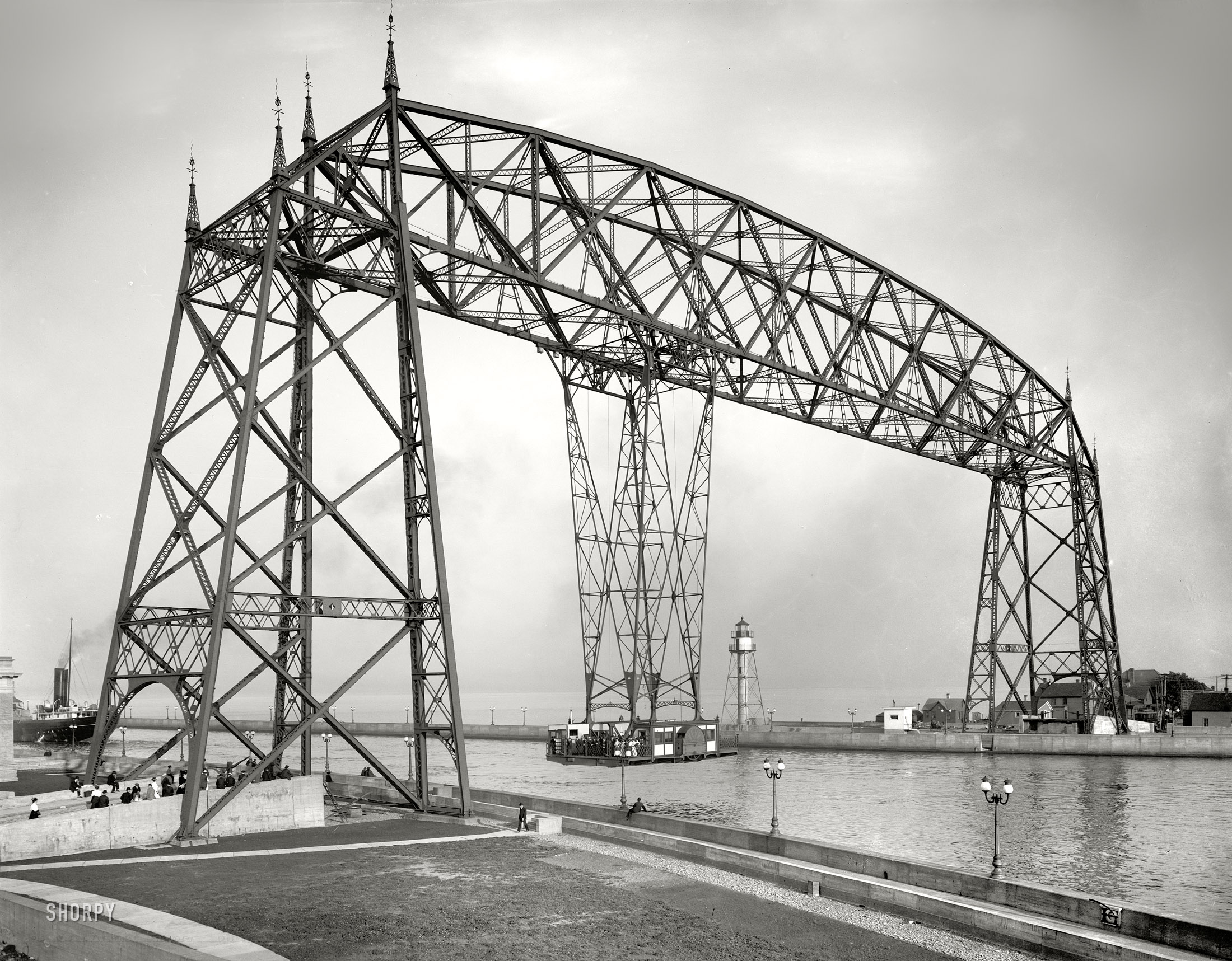 Circa 1907. "Aerial bridge. Duluth, Minnesota." Suspended Car Transfer over the Duluth Ship Canal. The gondola could carry 60 tons of cargo across the 300-foot channel with minimal obstruction of the shipping lane. After modification for service as a vertical lift, the span became known as the Aerial Lift Bridge. 8x10 dry plate glass negative, Detroit Publishing Company. View full size.