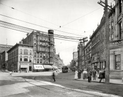 Grand Rapids, Michigan, circa 1908. "Monroe Street." Your headquarters for chatty chapeaux. 8x10 glass negative, Detroit Publishing Co. View full size.
Eliminates the middlemanNo need for a person to "talk through his hat." Now the hat can do the talking for him.
Nat&#039;l City still nearbyInteresting to see the National City branch at Pearl Street and Monroe. A modern branch is here in Grand Rapids just rear-right of the viewer. Monroe Avenue has changed over the years, from a road to a pedestrian mall, back to a road. Still a good variety of historic structures along its path, though the corner buildings and distant Herpolsheimers building are gone.
The lady in whiteThe city looks like a grimy place, but somehow the lady in the white -- or at least light coloured -- dress on the street corner manages to keep her apparel squeaky clean.
QuestionsOK, can anyone elaborate on "The Hat That Talks"? And the guy with the chair under the umbrella in the middle of the street -- a streetcar dispatcher?
IllusionsAs I scrolled across the enlarged version of this photo, I noticed the hat on the woman in white on the street corner. Did her hat have two tiny people on top of it? That would explain the talking hat part. No, it was people in the background, giving that illusion. As I scrolled down, I noticed the horse turds in the street and the fact that the woman was holding something that gives the illusion she is about to be hit by a flying horse turd (at least I HOPE it's an illusion). 
There she is in her lovely white dress, just waiting to cross the street, and 103 years later people are seeing tiny talking people on her head and large turd flying at her. It makes me wonder what people might notice about my own candid photos 100 years from now.
TodayThe photographer is looking basically southeast. The buildings on the right (south) of Monroe are mostly all gone; now Rosa Parks Circle is there, a downtown gathering spot for open-air concerts and ice skating in season.
View Larger Map
1908 DentistryBy the time you walk up 5 flights of stairs you will have forgotten about your toothache.
Talking hats serve an important purposeWhen you place one on your head, it tells you which branch of Hogwarts you are a member of: Gryffindor, Hufflepuff, Ravenclaw or Slytherin.
Umbrella (not) manre: Dennis M's comment: if you look at the shadows, you'll see that the guy bending over is several feet away from the chair, so I don't think the two are necessarily associated. I'd say it's more likely he's related to the overflowing trash can and broom at the curb - possibly collecting some detritus on the street. I'm going with your speculation that the umbrella/chair has something to do with a streetcar functionary.
[Perhaps the fellow over by the streetcar. Umbrella bears the name of Something Milling Co. - Dave]
(The Gallery, DPC, Streetcars)