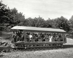 Holyoke, Massachusetts (vicinity), circa 1908. "An elevating car -- Mount Tom Railway." 8x10 inch glass negative, Detroit Publishing Company. View full size.
Self-LevelingThe gears and chain underneath the car enabled the car to "self-level" based on the underlying terrain such that passengers were always kept sitting upright relative to the slope of the incline, making the ride slightly more comfortable.
More than enoughI'm hoping it didn't take eight people to run this wonderful machine up and down the Mount Tom run.  And I'd move away from the fellow in the second to last row, he doesn't look too steady, if you get my drift.
Looks like funwww.mounttom.com for more info on this railway.
NOTICEAnyone smiling will be removed by the conductor(s) immediately.
The Place to BeOnce Holyoke was the place to be. It had an opera house, literary societies and stunning architecture. Indeed, some of New York's best architects from the early 20th century got their start there. And Mountain Park on Mt. Tom was a very fashionable summer retreat, even President Mckinley went there at least once. Holyoke's paper and silk based economy boomed until the end of the WWII.
Deindustrialization has hit Holyoke hard and the place now has a reputation of being a very rough town. But once it was really at the pinnacle of society in the Northeast.
ObedienceWith the exception of the ghosty lady in the first row of seats, it appears that almost everybody else sat still, looked at the birdy and didn't smile.
I Guess I Need to &quot;Brush&quot; up on LocomotionI can't figure out what purpose the brushes might serve on the bottom of the streetcar. Were they used for electric pickups or were they just for dirty boots? The wires along the top of the rails are also a mystery.
[The lower conductors are telephone wires. - Dave]
A clean track is a happy trackAnyone have any idea what the brushes are for at both ends of this car?
ExcessWant some tram with your conductors?
The brusheslook like they were a local modification, and they are outboard of the rail, so they're not there to clean it. They have a bonding wire running from them up into the car. So I'll make an educated guess and suggest that the car was prone to charging up, and the brushes were to intended to ground it at the carstops, to prevent the passengers from getting a jolt when they got on or off. More intriguing to me is the chain drive from the rear axle to the shaft at the centre of the truck - can't even begin to guess what that was for.
Uniform of the dayI count SIXTEEN people wearing uniforms, most seem to be conductors.
The brushes appear to be groundedPerhaps they're there to discharge static electricity when they reach the platform to avoid shocks?
Musical ConductorsI believe there are only two conductors, one driving and one at the back.  They have the same type of hats (double braid).  The other men in Nero collar jackets appear to be band members possibly arriving for the day's work at the top of the hill.
[I guess they'd be fiddlers, then. - Dave]
Safety brake sensor, not self-leveling chain driveThis is an intriguing semi-funicular trolley railway, unique so far as I can find, but there is virtually zero technical decription available of its design from the period, at least on the internet. Including the two Shorpy hi-rez photos there are only about a dozen photos in all, most fuzzy. And not a single photo of the summit's sheave 8 ft diameter unpowered pulley. Contrast that with the Lake George Catskills funicular, of which even the suppliers of each piece of the system are known, and line drawings available.
Yet the two Mt Tom trolleycars themselves are quite spectacular high quality designs for the period to my engineering eyes. They lasted forty years. So who was responsible? For my personal interest's sake, I have figured out how it all worked, which for an old retired mechanical engineer has been quite interesting to say the least. Thanks Shorpy for publishing these two photos in the first place. 
The chain drive from the railwheel axle through the bearing journal cover is to a governor shaft/regulator mechanism, not dissimilar to the Lake George arrangement by Otis which preceded this rail line. If the cable breaks, and the car runs away, the regulator senses the overspeed or reversal of rotation and activates the braking jaws on the car to grab the third iron rail and stop the car. Presumably it stops the electric motors as well.
The self-leveling argument for the seats seems to have been invented out of thin air by another blogger and repeated here. The seats themselves can be seen here to be pre-tilted so that they were more level when on the actual incline.
The brushes are the way only the Elizur Holyoke, which always took the left turnout at the bypass facing uphill whether ascending or descending, remained in telephone contact during the bypass phase of the journey. One brush arm is longer than the other to reach the appropriate wire - internal contact method unknown. 
Beyond the turnout bypass either up or down, both cars used the two wires to the right of the line facing uphill for telephone contact. And guess what? I cannot find a single photo of the main telephone wire contact system. Nobody seemed to photograph the right-hand side of either car. Ever. Other photos show different attachment arrangements of the brush arms to the EH car, so it must have been troublesome. 
No, the two trolleycars are not mirror images of each other either. Very clever indeed.
Some photos from other sources may be found here:
http://leonardjlosholyokehistory.blogspot.ca/2013/02/more-photos-of-holy...
(The Gallery, DPC, Railroads)