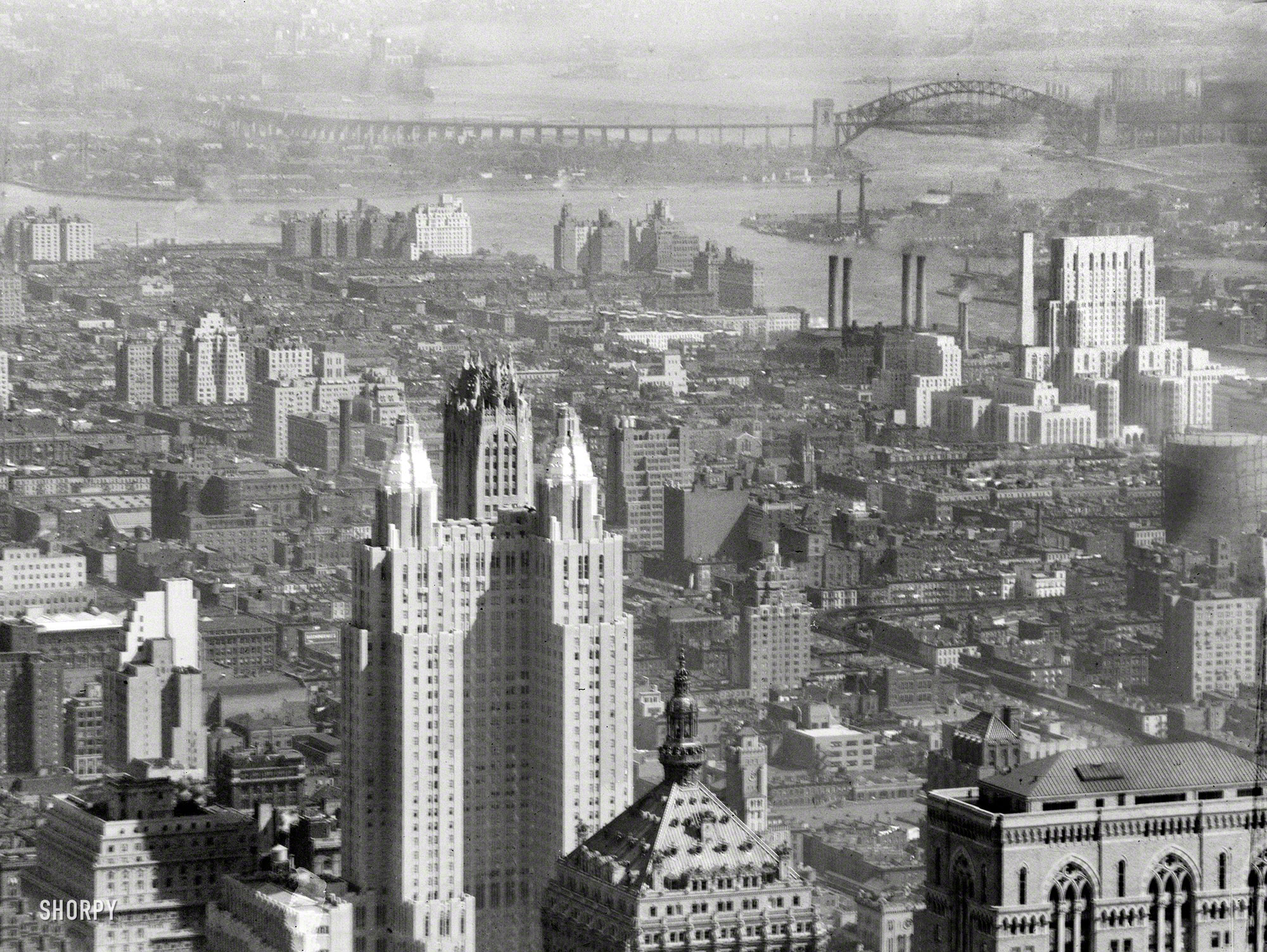 A view over 1930s Manhattan showing the Hell Gate Bridge across the East River in the distance, the Waldorf-Astoria towers and 230 Park Avenue (Helmsley Building) foreground, Lincoln Building lower right, and a gleaming New York Hospital on the right. 4x5 nitrate negative by Arnold Genthe. View full size.