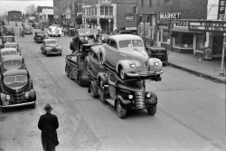February 1940. "Auto transport passing through Eufaula, Oklahoma." Now playing at the Chief: "Hunchback of Notre Dame." 35mm nitrate negative by Russell Lee for the Farm Security Administration. View full size.
CarspottingAs best as I can tell:  That's a load of 1940 Pontiacs being hauled by a circa 1939 GMC.  They're passing a parked 1938 Ford Standard.  Immediately behind them is a 1940 Dodge.  The car behind the Dodge is a 1938 Ford Deluxe or a 1939 Ford Standard (hard to tell at this resolution).  
Can any other Shorpyite identify the other vehicles in this picture?  If my dad were still alive (WWII Navy vet--happy Veterans Day, Dad!), I'm sure he could.
Product PlacementAmid the traffic, the Coca-Cola sign and the Pontiacs there magically appears a 7-Up delivery truck.
OKNot a quad cab pickup truck visible on an Oklahoma town's main street? How delightful. Town's folk drove what was practical back then. 
You like it, it likes youAnd I like the 7-Up delivery truck heading down the street. 
Classic vehiclesDefinitely a 1939 GMC hauling the load of cars. In 1940 American auto makers went to sealed beam headlights in place of the old bulb style and GMC had to put the parking lights which had been mounted inside the headlight buckets out on the tops of the fenders.The sedan delivery immediately to the right of the rig looks like it could be a 1933 or 34 Ford and the panel coming out of the side street (with the name TEEL) is  a mid 30s Dodge humpback. I love the fender skirts on the 7-Up truck body. Some classic vehicles. 
More carsBehind the '38 Ford is a '38 Oldsmobile, and beside it is a '39 Chevy.
Surprised no one has commented on the remnants of a marching band in uniform in the background of a shot (note the Sousaphone!) Wonder what the occasion was.
The Eufaula bandRussell Lee's photographs from that day did include shots of a short parade, in which a marching band was followed by a few gentlemen giving rides to others in wheelbarrows.  The notes from the photos in the Library of Congress archives gave no clues of the occasion, but the local newspaper did.  According to the Feb. 15, 1940 Indian Journal (the official publication of the City of Eufaula, Oklahoma), the local Jaycees were planning a "Street Comedy Act," including a marching band, as the culmination of competition between two teams to increase the chapter's membership. The "comedy act" would involve having the losing team's members giving wheelbarrow rides to the winning team's members. 
How&#039;d they do it?How'd they get the car over the transport cab up there?
[I'm guessing a ramp. - tterrace]
Probable loading sequenceThe car over the truck cab was loaded first, using the ramps to bridge the gap between the top of the rear ramp and the truck cab. The middle car was loaded next and the car in the back was loaded last. It took a lot of shifting of the ramps around. I wonder how many cars were damaged during loading and unloading in those days
One moreI believe there is one more new car inside the trailer underneath the top rear car. It has a cover over it to protect it from debris kicked up by the tires of the truck.
Dad&#039;s hangoutMy father was about 8 years old and living in Tulsa when this photo was taken. His Aunt Bea (and other relatives) where of Creek heritage and lived in Eufaula at the time. From time to time, he would get to go to Eufaula and visit her for a weekend, or maybe spend a couple of weeks during the summer down there with her. He always spoke fondly of these trips and had a special place in his heart for his aunt. Many of our Creek relatives are buried at the cemetery there near the main highway.
(The Gallery, Cars, Trucks, Buses, Movies, Russell Lee)