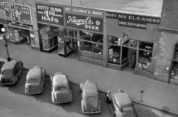 October 1940. "Grand Forks, North Dakota." 35mm nitrate negative by John Vachon for the Farm Security Administration. View full size.
A different use for grainInstead of selling beer, that location is home to a bakery. The Dotty Dunn hat store was at 17 N. 3rd Street. It, the bar and the dry cleaners are all gone, even the cut rate store to the left. The only building that survives is the one to the extreme right. Which appears to have a barber shop. BTW, Dotty Dunn Hats was a chain store operation.
View Larger Map
BarrenOnce again, like the Chicago photo, few people and an angle chosen that makes it seem that you're looking down on a detailed area of a really cool O-gauge layout. Perhaps that's what Vachon was trying to capture.
Bull City Boy has a great question, what is that automobile?  A totally different look from the others. I haven't clue alas, [Lincoln Zephyr?] but now I gotta find out.  What is it? 
Anywhere, U.S.A.Nostalgic picture which is so similar to the small town in which I grew up but on the East Coast. Our businesses on Main Street (with the same kind of diagonal parking before meters) were Carroll Cut Rate, Adam's Hats,Gene's Bar featuring Rheingold beer, Pete's Barber Shop and Bashura's Shoe Repair.  I used to love the fumes in the shoemakers and cleaners, both now deemed very lethal, i.e. shoe polish, glues, leather-tanning chemicals and carbon tetrachloride. We also had a Hart's Five and Dime and a First National grocery. Kind of neat to think that whether you grew up in the East or Midwest, the small town Main Streets were so similar.   
Brew NotesAs a side note, Kiewel's Beer was brewed in Little Falls, Minnesota, while Heileman's Old Style (hanging sign over the tavern door) was brewed in La Crosse, Wisconsin.
Interior HingesSo, is no one going to identify the autos, especially the fourth from the left?
P.S.  I've been away for five weeks. Glad to be back and I'll be catching up with Shorpy as best I can.
Inflation$1.98 in 1940 would be about $32 today.  Not a bad price for a man's hat.
Cars ID&#039;dFrom left,
1940 Chevy with deluxe rear center guard.
1937-38 Chrysler
1937 Nash
1939 Chrysler?
1940 Oldsmobile
Comments welcome. 
The vehicle 4th from the left is a 1939 Ford Deluxe 2 door sedan. Better later than never.
(The Gallery, Cars, Trucks, Buses, John Vachon)
