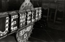 October 1941. Chillicothe, Ohio. "Jewelers sign." 35mm nitrate negative by John Vachon for the Farm Security Administration. View full size.
The stuff that dreams are made ofJust the thing Spade or Marlowe would see from his office window.
Mis-spelling?Null points for spelling - both you and the sign maker - Jeweller surely?
[In American English, "jeweler" has but one L. - Dave]
Little light bulbsIt must have been a major job keeping signs illuminated in the pre-neon days.  Now even neon is passe -- being replaced by LEDs (Light Emitting Diodes).
[Neon -- replaced ages ago by fluorescent backlight signage -- is actually quite chic these days. - Dave]
Yes, I never liked fluorescent back-lit signs, they are bland, boring. Neon was more colorful and can be animated.  LEDs are more colorful and animateable yet- and can create infinite designs and even pictures.
Cool sign, cool photoI think John Vachon took by far the most interesting photographs of anyone from the FSA.
De-signsSome of these signs were pretty cleverly designed.  The garage sign below is one of my favorites.  It sold for $34,500 at auction last year.
(The Gallery, John Vachon)