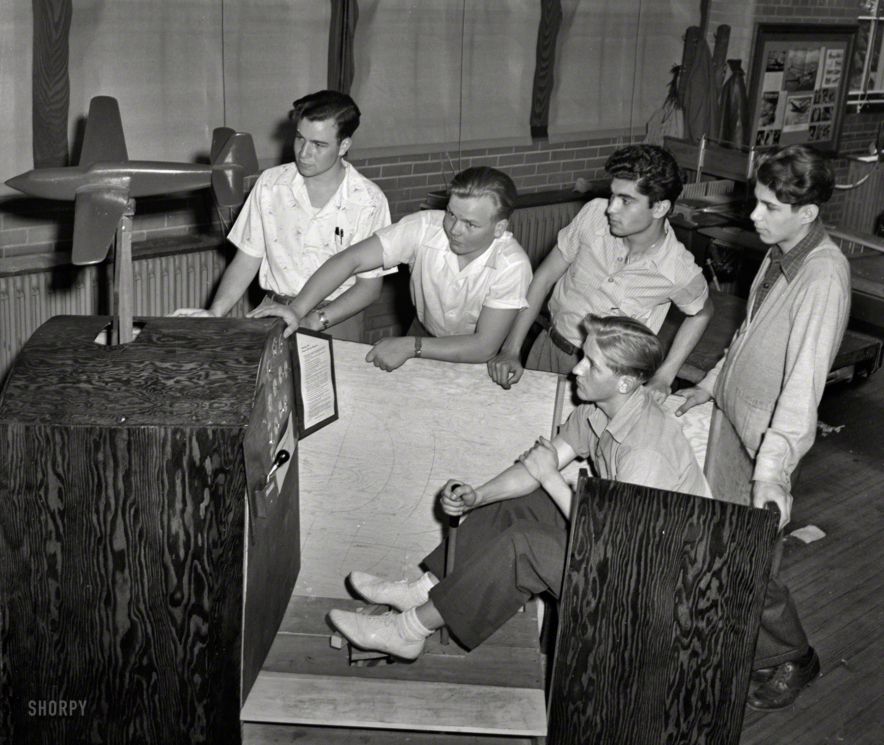 July 1942. "These high school boys constructed this trainer plane, and the young man holding the stick is operating it. Note the instruments and control board. This is one phase of the aviation course offered boys at the Weequahic High School in Newark, New Jersey." Text in the cockpit: "Getting the Plane Off the Ground." Office of War Information, photographer unknown. View full size.