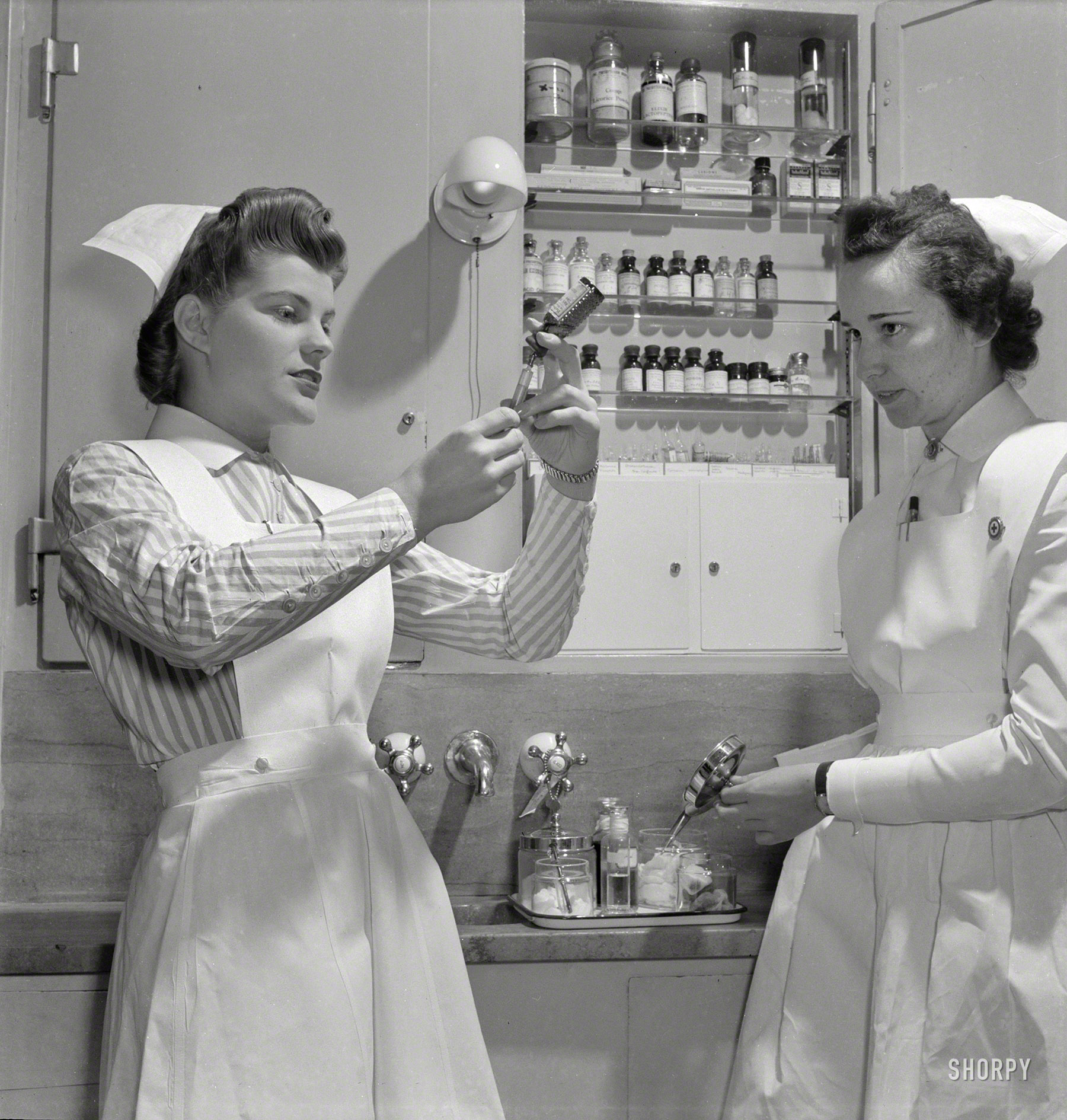 November 1942. "Nurses in training. Babies' Hospital, New York. A graduate nurse (right) watches student Susan Petty prepare a hypodermic for a patient. Strict adherence to doctors' orders is something every probationer must learn." Photo by Fritz Henle for the Office of War Information. View full size.