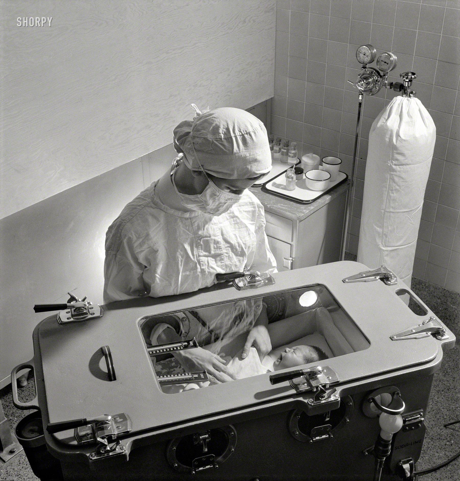 November 1942. "Babies' Hospital, New York. Care of prematurely born babies is one of the most complicated procedures which must be learned by the student nurse. Feeding, bathing and diaper changing are carried on inside the incubator, in which temperature, humidity and oxygen must be carefully regulated. The oxygen tank can be seen in the background." Photo by Fritz Henle. View full size.