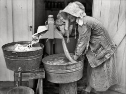 May 1938. Irwinville Farms, Georgia. "Mrs. Coleman doing a washing." Slow but steady progress in the science of mechanized laundry. Medium-format nitrate negative by John Vachon for the Resettlement Administration. View full size.
Pre-wash perhaps? I see what looks to be a portable washer on the other end of that wringer actually driving the rollers. She is probably either pre washing the sheets or just doing them by hand to save electricity. Use it up, wear it out, make do or do without. They were a necessarily frugal bunch back then, and would be dismayed, I think, at the waste and profligate abuse of resources occurring today. But I still wouldn't trade places with them.
Laundry is so easyI do other things while the clothes are washing but I remember one of these machines in the basement as late as 1967.  BTW, I think this photo needs a "pretty girls" tag with that lovely face and smile.
Is she wearing a pair of Red Ball Jets?
Wringer useI thought the wringer was used for removing water from your clothes.  Yet both her buckets are full, and the presumably clean laundry is headed into a full bucket of water?  Am confused.
[She's wringing out the soapy water. - Dave]
The Wringer WasherOur Mother had a wringer washer well into the 1940s. An Easy. Here's the drill: Fill washer with hot water and soap.  Add dirty clothes. Let washer agitate for how many minutes you need. Drain washer into laundry sink. Run soapy clothes through wringer, place back in washer. Fill washer with clean water, agitate again. Drain washer, and wring clothes again. Shake out each piece and hang on clothesline. A lot of work, but it sure beats a scrub board.
Not Just Another Pretty FaceEverything in this picture conveys a hard life and then there's that pretty, smiling face. Her expression changes the whole picture.
Under That Bonnet Is a beautiful woman.
WringersMy grandmother used one of those into the mid 1970s.  She had it on the back porch between two sinks just like that.  She was a child of the depression and there was no reason to spend money on new-fangled washing machines when the old wringer worked fine.  Hers was electric if I recall.
Don&#039;t Waste the EffluentOld-timers have told me that the phosphates in the old laundry soaps made the waste water useful as fertilizer.
Work saverI have done laundry by hand a few times and the hardest thing about it, by farm was wringing enough water out by hand so that things could dry before bacteria would start to grow in them.  I've also used an old wringer washer, and the wringer made an enormous difference! I'll bet Mrs. Coleman had done plenty of laundry by hand and was very thankful for that electric wringer!
Is she wearing Why not? They were generally considered "po' folk" shoes back during the Depression. I think that Chuck Taylor designed them during the 1920s.
Just a non-scientific pollI wish I could know how many of us Shorpy viewers couldn't resist smiling back at this lady smiling at us. What a nice way to start my day.
Don&#039;t Waste the EffluentActually that was why it was banned in the 1970s and later. The phosphates got into the sewer water and eventually into the ground water. In rivers and (locally) the Great Lakes, it led to algae blooms that killed off fish and damaged the quality of the drinking water.
Jealous of Mrs. Coleman&#039;s water faucet.At least Mrs. Coleman didn't have to draw all that water out of a well, bucket by bucket, like we did.  Also, there had to be a fire built in the yard to heat the water.  Wash the clothes in the washer, wring out and into the first tub of rinse water, wring out again and into the secont tub of rinse water.  I hated washday until I was sixteen!
(Technology, The Gallery, John Vachon)
