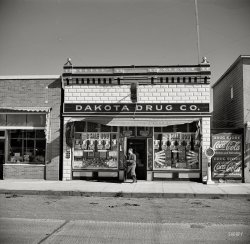 October 1937. "Drug store. Stanley, North Dakota." Medium-format nitrate negative by Russell Lee for the Resettlement Administration. View full size.
Could this bethe same place?
Am I misreading the evidence?I'm not absolutely certain, but there might be a 1¢ sale going on.
Tincture iodine sale! When was the last time you heard of someone using that stuff? 
A dipoleIt looks like a dipole antenna, above the store, and the single visible end support even has insulators in its guy wires.  I'm guessing the store to be about twenty feet wide, so the dipole's full length would be about forty feet.  That would make it resonant around 12 megaHertz, but I'll bet the feedline is balanced (using two wires), making the whole feedline-antenna system tunable.
There's a ham radio operator in that drugstore!
RE: A dipoleThere must be a butcher shop out back, which would explain the "ham" radio setup.
(The Gallery, Russell Lee, Stores & Markets)