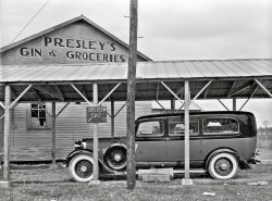 January 1939. "Funeral ambulance parked under gin shed. Mound Bayou, Mississippi." Photo by Russell Lee, Farm Security Administration. View full size.
The Presleys of MississippiSeem to all be related quite closely. Anglicized from the name Bresslar they settled first in NC, then TN, and finally MS. There were related Bresslars, Presslars, Pressleys, and Presleys so it is easy to differentiate between the branches of Elvis' family.
This information comes from an Australian website (figures, don't it?).
Get a Handle on ItI guess the Funeral Car driver had to enter the vehicle from the passenger side.
Good EyeThe Case of the Missing Door Handle. It's the wee details that are the real charm of SHORPY.  That hearse looks quite well taken care of except for that little detail.
I have to askAny relation to someone famous from Tupelo, Mississippi? 
The hearseThe hearse appears to be a McCabe-Powers body modification of a 1934 Lincoln KB, making it about five years old when this photo was taken.
Based on the slight sag in the rear end and the visible compression in the rear tire, I'm wondering if the rear compartment was occupied at the time. It might just be aging suspension and a slightly underinflated tire, but you never know...
The funeral directorThe hearse belongs to Powell's Funeral Home of Mound Bayou.
Hybrid HearseThis hearse is comprised of components from multiple different automobiles.  It is definitely not a Lincoln from 1934 as suggested below.  
The grille appears to be from a 1930 Lincoln or earlier as 1931 and later grills had a slight bow to the front.  The 1934 Lincoln grille was body colored.
The hood doors on Lincolns had straight sides only in 1932, and these hood doors don't look like they were produced by Lincoln.  The 1934 Lincoln hood doors were canted towards the back of the car.  The 1930, 1931  and 1933 Lincolns didn't use hood doors.
The wheels and hub caps are from a 1931 Lincoln, at the latest.  The 1932 - 1934 hub caps covered the bolts and lug nuts that hold the wheels to the axle.  The painted black circle detail on the hub caps was only used in 1931.
Although the front fender looks close to those manufactured by Lincoln in 1934, it lacks the minor upsweep that went from the driver's door towards the front wheel.  In general, the front fender looks too big and seems out of place.  The parking light is also missing from the fender.  The rear fender does not look like a Lincoln fender from any year.  
The height of the chassis cover plates, the area between the bottom of the doors and the top of the running boards which was quite large in 1930, provides another clue that the chassis is not from 1934.
(The Gallery, Cars, Trucks, Buses, Russell Lee, Stores & Markets)