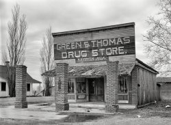 January 1939. "Vacant drugstore. Mound Bayou, Mississippi." Ballad of the sad pharmacy. Photo by Russell Lee, Farm Security Administration. View full size.
WowA hand-split shingle roof, don't see too many of them these days.
Why Was It So Unusual?Selling Hollingsworth's Candies. Maybe this is why Green &amp; Thomas went out of business.
Sign Painter, Drugs and GasolineIt says "Wallis 11-26-29" under the drugstore sign. Wallis was probably the sign painter and he did his artwork in November 1929, 10 years earlier. Also the three columns might have supported a portico. Was the building a gasoline station before it was a drug store?
Ten years afterThe sign painter's tag shows 1929, and the photo 1939. Between the brick posts appear to be gas pump mounts. Apparently the addition of fuel sales couldn't help this establishment. Probably should have called out the sign painter to update up that sign.
Unusual Candies!I've never heard of Hollingsworth Candies, but here's the back of one of their candy boxes (found via Google) describing what's inside. Evidently they were located in Augusta, Georgia. 
The grand-daughter of the founder posted on the site where I found the box image, and another relative of a long-time employee there stated she had the company recipe book. Pretty nifty in case you crave a Crispette!
That is such an interesting photo; the front door appears to be open, and I can't imagine what the purpose of those three bricked columns was. Could gas pumps have been between them? Looks like something was.
Out on Old Hwy 61Mound Bayou is oldest all-black town in U.S., founded in 1887 by ex-slaves from a local plantation.  More info here.
Sole OwnerAs such, alas, B.A. Green cannot blame an unimaginative board of directors or a peculating CFO for the demise of his business.
(The Gallery, Russell Lee, Stores & Markets)