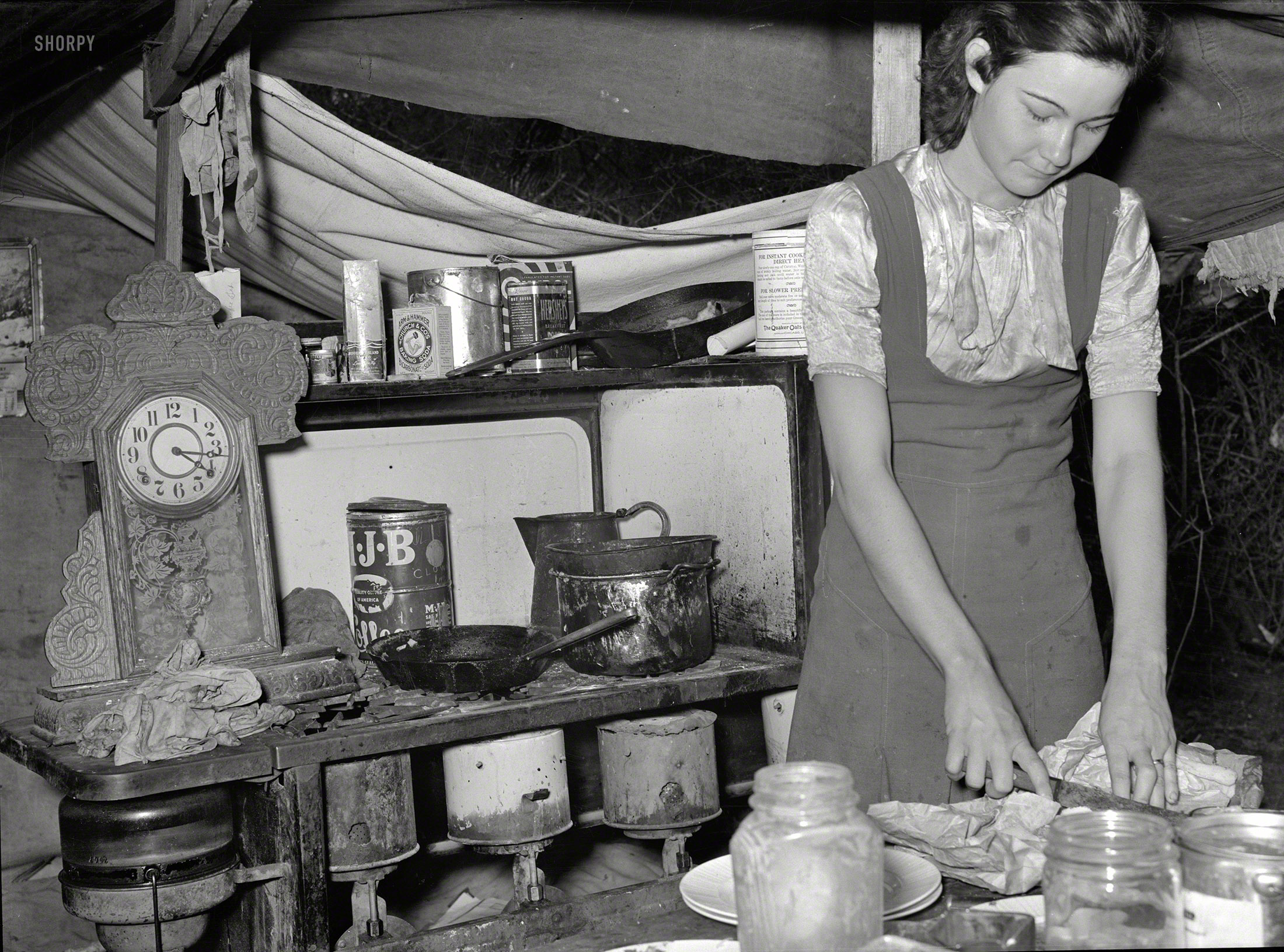 February 1939. "Kitchen table and stove of white migrant tent camp near Harlingen, Texas. Married daughter of migrant worker cutting salt meat for dinner." Medium-format nitrate negative by Russell Lee. View full size.