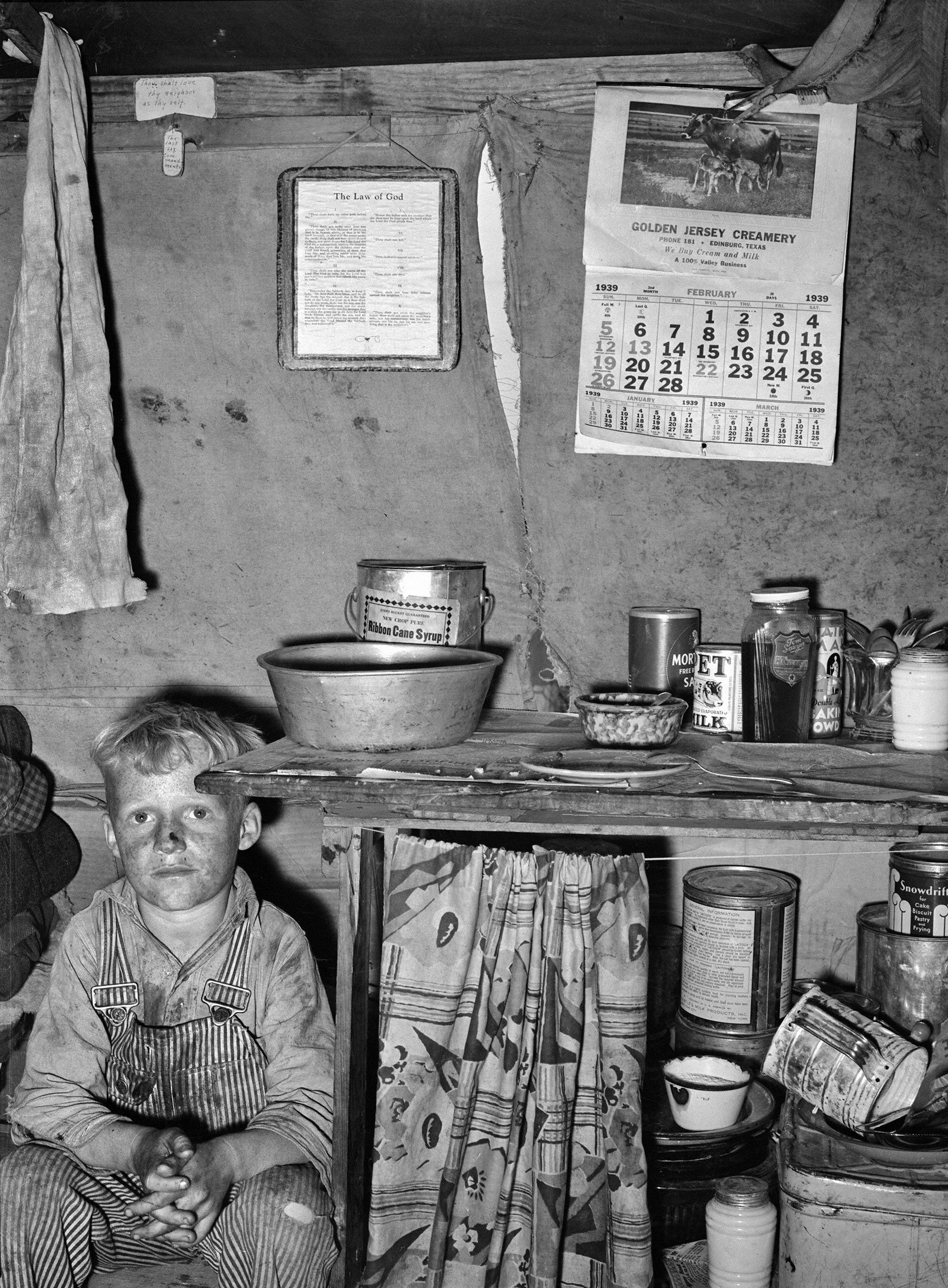 February 1939. "Child of migrant sitting by kitchen cabinet in tent home near Edinburg, Texas." Ten Commandments, meet Jersey Creamery. Medium-format negative by Russell Lee for the Resettlement Administration. View full size.