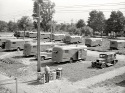 June 1941. Erie County, Pennsylvania. "Each group of ten trailers in the FSA camp at Erie has a trailer service unit, water faucet, slop sink, and garbage pail." Photo by John Vachon for the Farm Security Administration. View full size.
Car make?Ok, what is the make of that car on the right side of the photo?
[Appears to be a 1930 Durant. - tterrace]
You nailed it: 1930 Durant Model 614 Standard sedan. Thanks.
Yep, a Slop SinkDon't think I was aware of the headline term until some years ago when I bought some plumbing part to repair a fixture in my house, and was warned in the instructions, "Not for use in slop sinks."  Have loved the concept ever since.  The man in the photo appears to be cleaning a bucket in the slop sink, rather than installing any forbidden fittings, so he should be safe.  Intriguing image from the days when '41 Pontiacs still rolled the earth.     
Can on the SideNo coolant recovery sytems on that old Detroit iron back then. So between boil overs and leaky radiators, water pumps,etc. a good water can was a must. 
Home Sweet HomeThat it was, for myself, Mom and Dad, for about three years in the 1940's. I believe these are the Schult trailers. (http://www.coachbuilt.com/bui/s/schult/schult.htm
We had the short model near the camera, but only one heater near the door. The trailer had only two tempertures, too hot and too cold!
(The Gallery, Cars, Trucks, Buses, John Vachon)