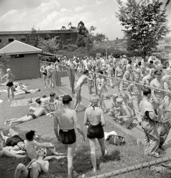 July 1942. "Sunbathers on the grass next to the municipal swimming pool on Sunday." The pasty white underbelly of wartime Washington. Medium format negative by Marjory Collins for the Office of War Information. View full size.
Men&#039;s swimwearThrough the mid-1930s, tank tops seemed to be standard swimwear for me. By the early 1940s, nearly everyone wore trunks. Am I correct in thinking that the change happened very quickly? What caused the change in fashion? 
Pasty WhiteIn the 1960s I had the honour to serve in the US Navy at a sub base in Holy Loch, Scotland. After having been there for 18 months, my ship the USS Simon Lake was relieved by another, the USS Canopus. I transferred to the Canopus for another tour. Some of my new shipmates asked me how come I was sooo white. I pointed out that there was little sunshine in Scotland, and shortly they would be just as pasty, too.
Long story short, a nice tan was not a very important thing in 1942, unless you were Cary Grant.
More Men&#039;s Swimwear10 and 15 years later, in the mid 1950s, when I was old enough to remember swimming pools, these lads, grown up and now fathers, were still wearing those Superman trunks. We kids, however, were stuck with little children's boxers.
Those were Philadelphia and South Jersey memories.  A New York City friend says that up there, male swimmers went directly from old fashioned suits to boxers.
An urban legend is that a wartime shortage of cloth brought the end of coverup suits and also the arrival of bikinis.
Casual, almost indifferentWhat strikes me about this photo is the casual atmosphere of the scene. One might not realize a war was underway - the previous month, the US Navy had fought the critical battle of Midway.
The soldiers depicted in this photo have the casual, even sloppy appearance (headgear at improper angles; collars loosened, etc) of clerks assigned to DC area offices. If they had been recent trainees, one would hope that the spit and polish regime was still present.
Photo might be captioned: "At ease on the homefront".
I&#039;m Not a Big FanI'm just a little one with an oscillating gear drive, silhouetted inside the little window of the frame shack.
Pool Pass?Are the GIs just taking an opportunity to wander by the pool, sightseeing, or has the USO or other agency arranged for pool passes? If anyone knows which way the entrance is from this shot, maybe it would help figure that out.
Since it's early in the war, the U-boats are working right off the coast and probably more than one GI is thinking, "Hmmm, maybe I ought to work on my backstroke?" These guys knew they most likely weren't flying anywhere to fight, unless it was in a warplane going overseas, too.
The pasty white underbelly of wartime WashingtonImagine where all those guys in Army uniforms were eventually to go.  They look so young.
But then I was 18 years + 3 months when my turn came.
LeanWe were certainly a trimmer nation.
Men&#039;s SwimwearSewickley, I made the same comment several weeks ago when there were swim pictures from 1939 and then right after the war. In the pre-war pictures all the men had swimsuits with tops and after only bottoms. I guessed that perhaps it was because GI's bathed in just their shorts and when they came back it just carried over. However it appears the change was even quicker (as you commented) as this picture in 1942 shows only one male with a swim top. I am like you curious as to what caused the change. Perhaps we have someone from the fashion industry that could answer this question.
[Googling {men's swimwear history} gets you off to a good start. - tterrace]
Pasty White IndeedAnd the brothers and sisters would be swimming ... where, exactly?  Not to be more than usually preachy, but this shot is a pretty good indication that such places in our nation's capital were still segregated back then (like military units, housing areas, and almost every other public facility).  It is fitting for Americans of all races to remember that the good old days were replete with bad features and that, as a people, we have indeed come a long way since then.
Back of the subBuilding in the background is now the U.S. Park Police Central Substation.
July in DCJuly in the District of Columbia can be blisteringly hot.  It can easily reach 100 degrees that time of year.  I'm amazed that the guys in uniform don't look a lot sloppier.
SW DCIf you look a little to the right of the lamppost you will see the USDA building, which runs along C Street SW from 12th to 14th Streets.  The pool must have been near where 12th Street merges into Maine Avenue.  The lanes of I-395 run through the location today.
SwimmingI think this is the building.
There is a pool here too.
LocationEast Potomac Pool on Hain's Point is probably where photo was taken.  Same location as ball game with UFO in background, boy and girl with bikes lying on grass and two girl swimmers.
East Potomac ParkYes, thank you, you're right.  My range estimate was way off.  It's across the channel in East Potomac Park.  
The pool may have been a WPA project.  People could swim in the Tidal Basin until the late 1920s.
Top of Washington MonumentThe top of the Washington Monument can be seen in the background.  Here's a 1934 photo of the top:
(The Gallery, D.C., Marjory Collins, Swimming)