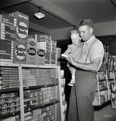 May 1942. "Greenbelt, Maryland. Father and son shopping in the cooperative store." Next, kid, I'll teach ya to shop for tobacco products. Photo by Marjory Collins for the Resettlement Administration. View full size.