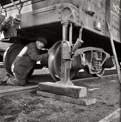 November 1942. "Chicago, Illinois. Jacking up a car on the repair tracks at an Illinois Central Railroad yard." Someone get the spare out of the trunk? Medium-format negative by Jack Delano, Office of War Information. View full size.
RIP: 1942Delano caught it on one of the RIP tracks. Repair In Place.
Treble MemoryI believe both wheels shared a common axe. So  to make a change he needs another jack. Quiz time: why were the outer rims tapered?
[That axe never stops sharpening. - Dave]
Doh!When they told him to go get a Duff he thought they meant Beer.
Not just trucking aroundThere probably is another jack out of view to the left.  He'll be removing the whole truck (both axes...er...axles and all 4 wheels).  If he was just removing one pair of whhels he'd have to support the truck somehow instead of the frame of the car.
Don&#039;t Damage the FinishWe first saw a track jack and Texas toothpick back here. I don't quite understand the padding that seems to be sitting on the business end of the jack. 
Tapered wheelsTapered wheels keep the wheels centered on the rails and allow for the different distances each wheel travels when going around curves since they have a solid connection via the axle to the opposite wheel. In an ideal world the flanges should never touch the rails in reality they do however.
Wheel taperWheel taper is 2 degrees 50 minutes.  The taper is designed to keep the flanges off the rail heads and to eliminate hunting. The wheels are pressed onto the axles. This particular car has 33 inch wheels and plain bearings.  It would be another 20 years before roller bearings were in widespread use on freight cars. 
That guy has some &quot;get up and go&quot;Now that's what I call a faith-based initiative!
That JackThat jack is very similar to the ones my father had stored in his garage. He used a couple to jack up the front and back porches on his house (for long term stability). He called them "house" jacks, and I'm sure they are still doing their jobs 60 years after installation!
Trucks and solid axles. With the solid friction bearing axles as in this pictured truck. The truck needs to be disassembled to replace a wheel set (2 wheels and axle). The paper between the jack and steel body is to reduce slipping of the steel on steel surface. 
(The Gallery, Jack Delano, Railroads)