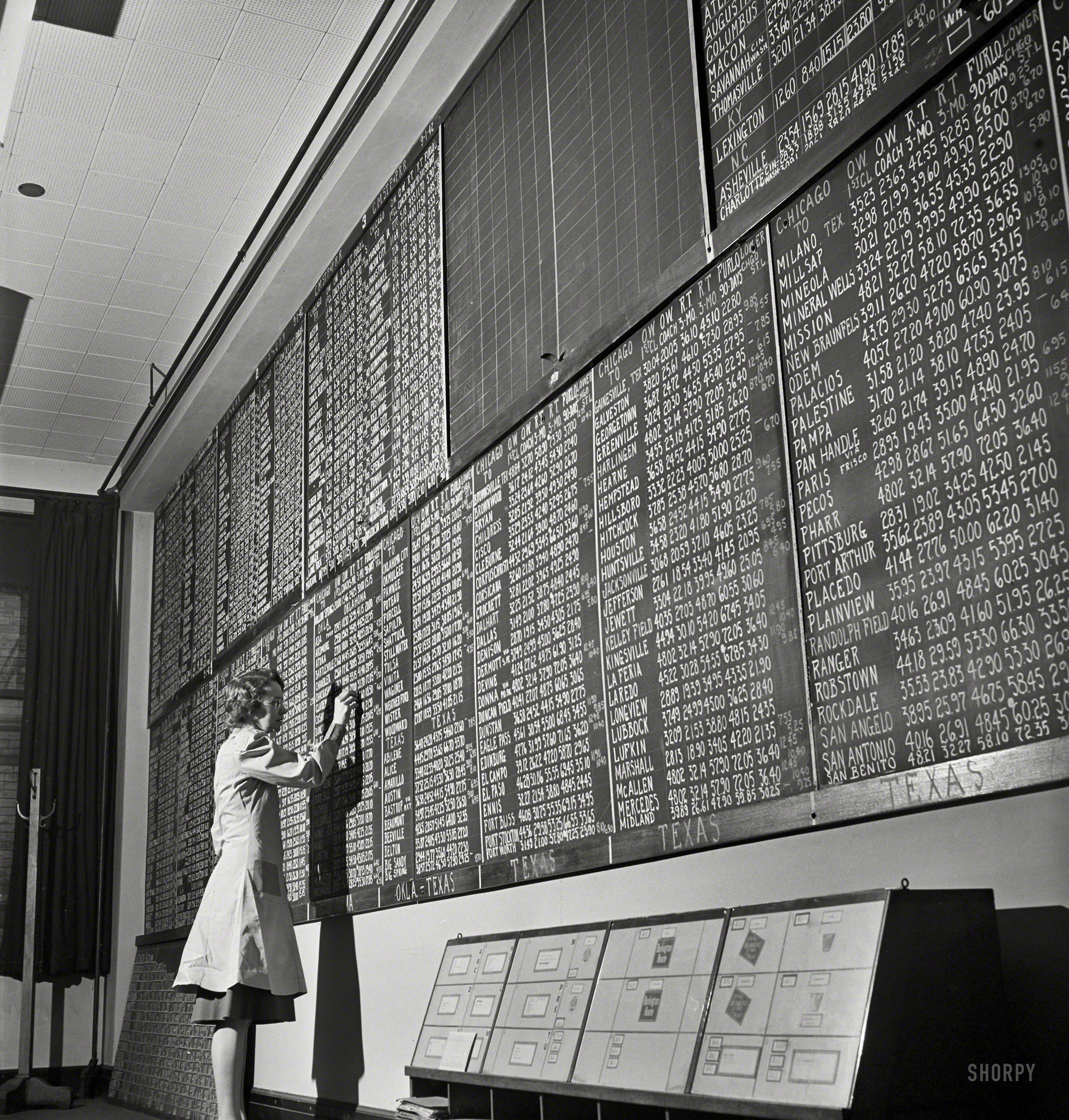 January 1943. Chicago, Illinois. "Mrs. Marie Griffith, manager of the information room, at one of the boards listing rates to points all over the country at the Union Station." Photo by Jack Delano, Office of War Information. View full size.