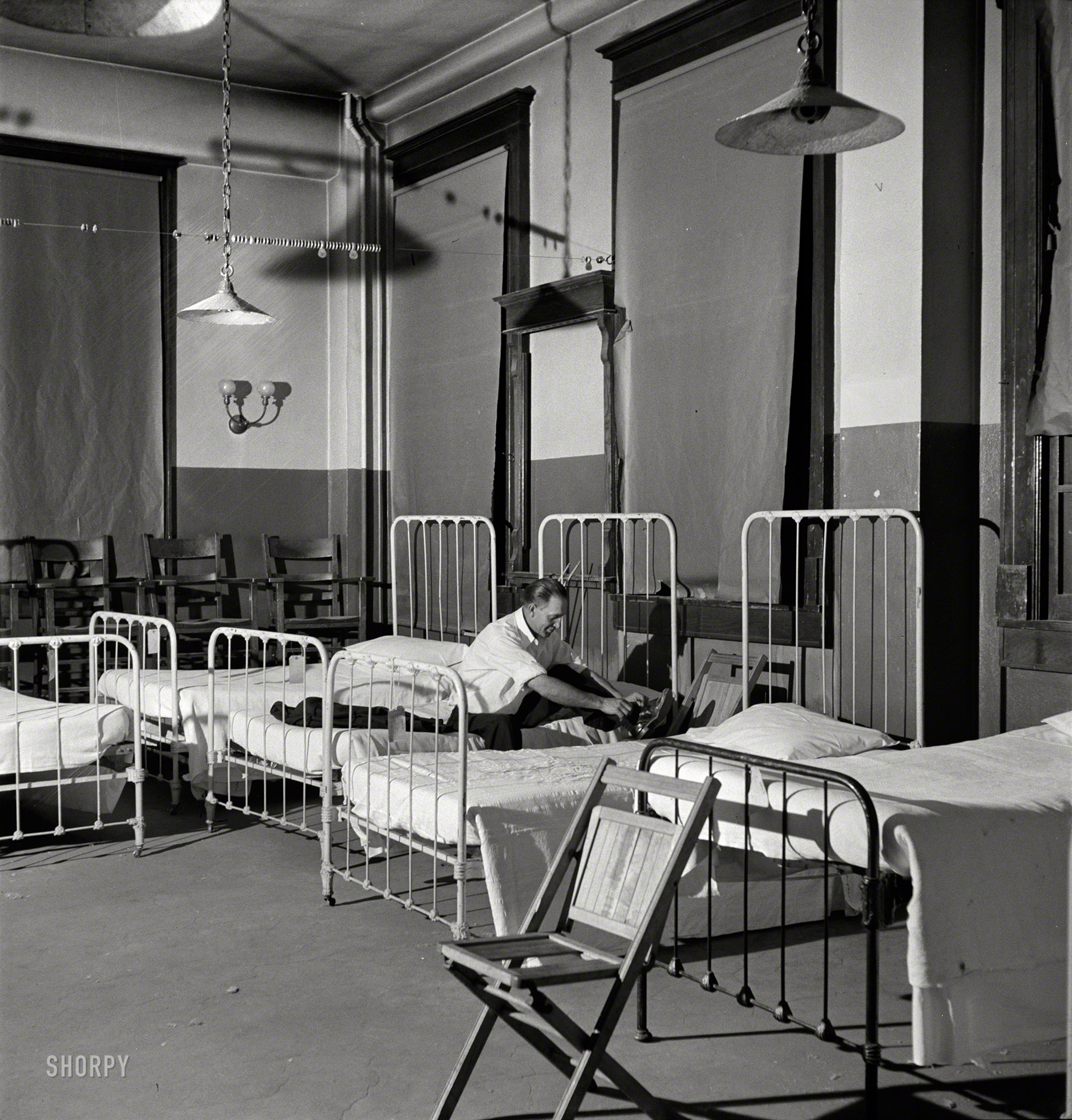 March 1943. Barstow, California. "Brakeman Thurston H. Lee (whose home is in Chicago) going to bed at the reading room in Barstow, California. This room has been converted from a billiard room into a dormitory at the Atchison, Topeka, and Santa Fe Railroad yard." Medium-format safety negative by Jack Delano for the Office of War Information. View full size.