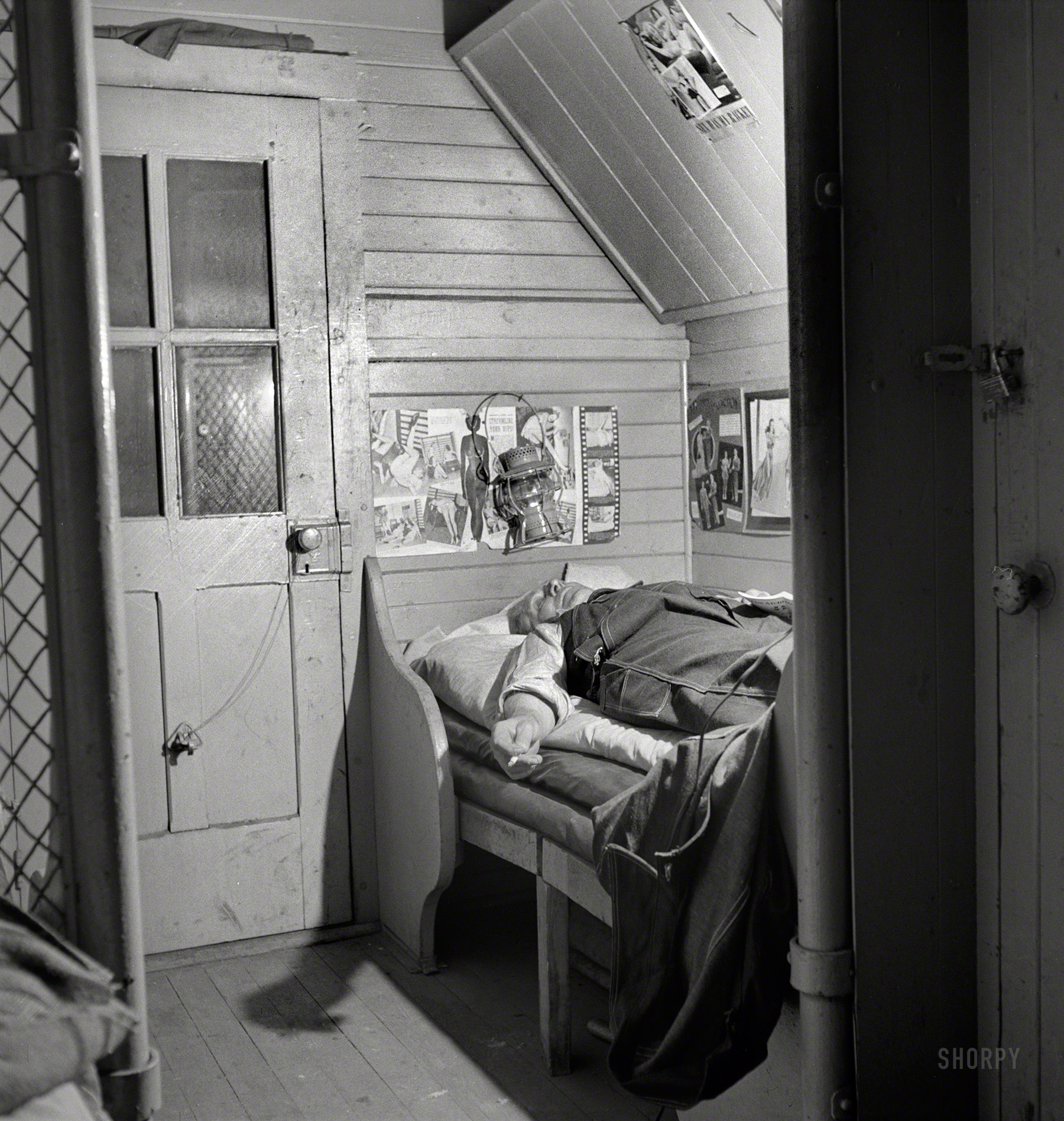 March 1943. "Barstow, California. A brakeman on the Atchison, Topeka and Santa Fe Railroad resting in his caboose at night." Pinup reading material includes: STREAMLINE YOUR HIPS! and SEX WAS MY RACKET. Medium-format safety negative by Jack Delano for the Office of War Information. View full size.