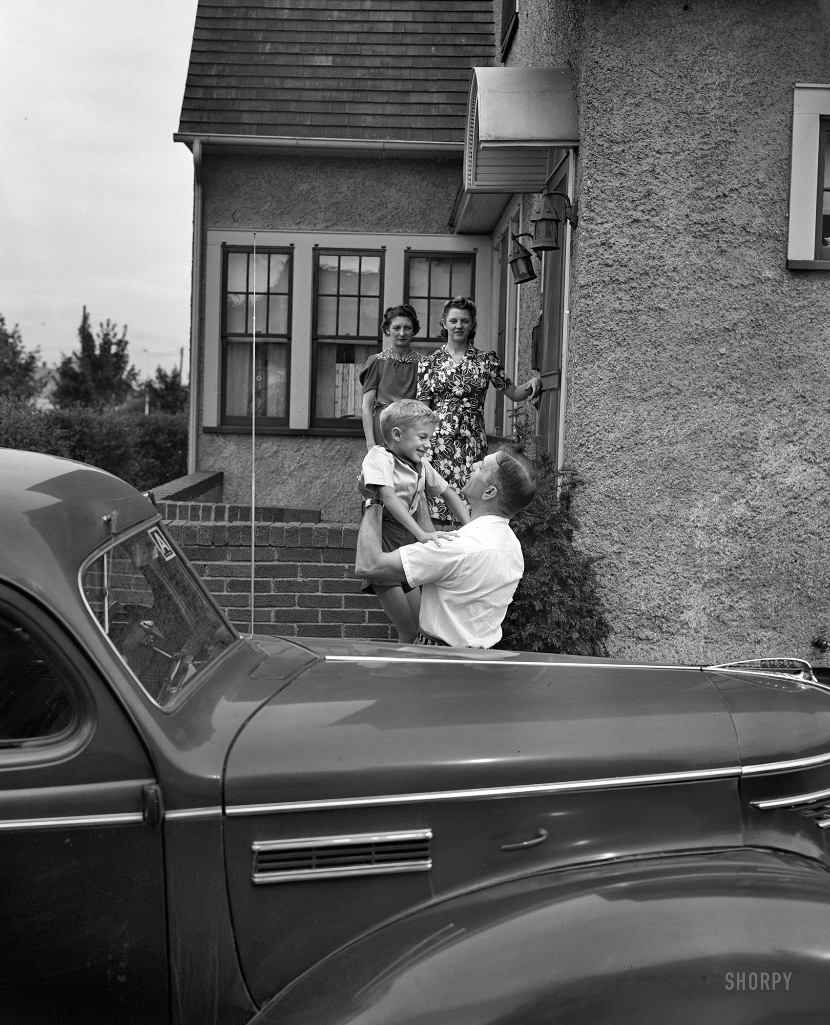 September 1942. "Rochester, New York. Mrs. Babcock, Shirley and Earl greeting Mr. Babcock in front of the house." The nucleus of this nuclear family, orbited by his little electron. Large format negative by Ralph Amdursky. View full size.