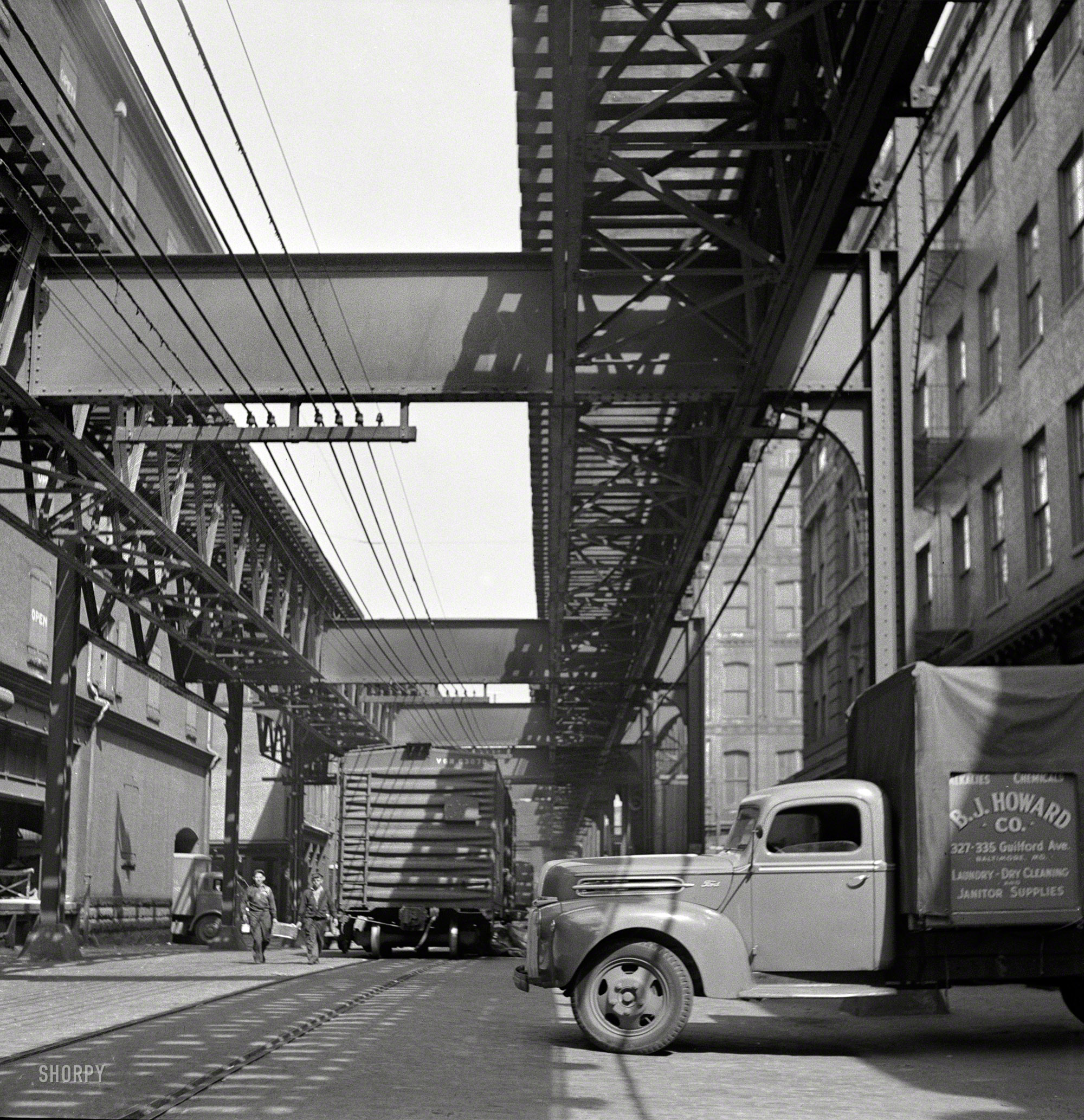 April 1943. Baltimore, Maryland. "Trucks and trains unloading goods underneath elevated trolley." Medium format negative by Marjory Collins. View full size.