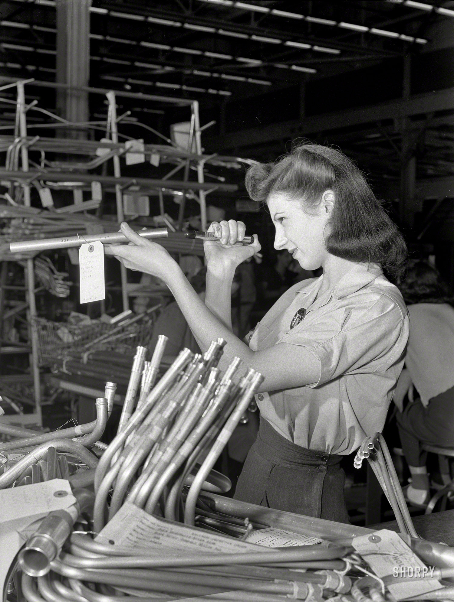 July 1942. "Ford bomber plant at Willow Run, Michigan. Inspection of more than a thousand separate tubing pieces composing the fuel, hydraulic, de-icing and other systems in a bomber is a highly important job. This young employee at the giant Willow Run plant uses her tiny flashlight to discover any internal defects in the tubing." Photo by Ann Rosener, Office of War Information. View full size.