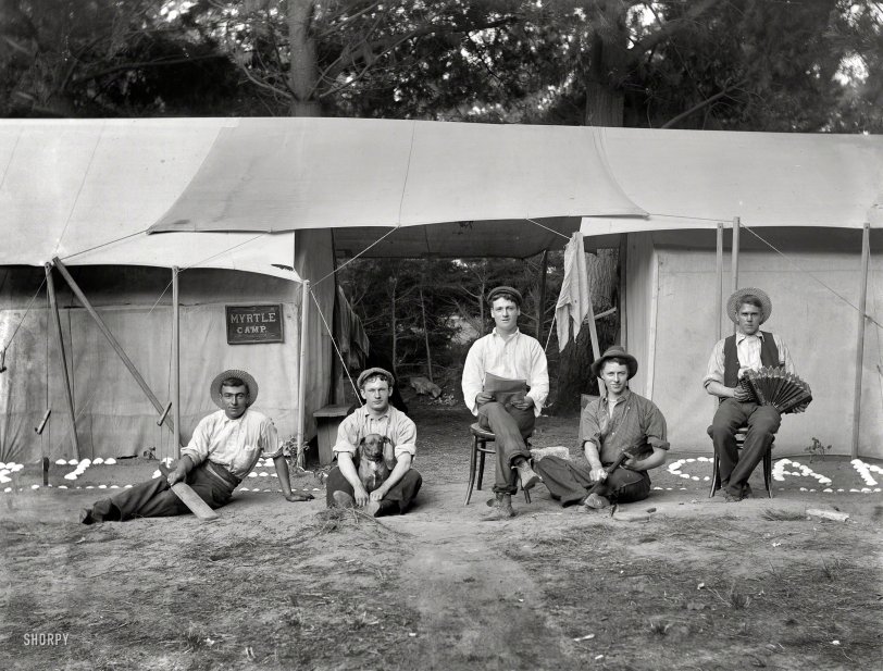 Circa 1905 in Sumner, New Zealand, a coastal suburb of Christchurch. One of 10 glass plates by the photographer Adam Maclay showing the denizens of "Myrtle Camp," possibly over a span of years. These fellows are always up to something -- their recreations included cricket (we hope), playing with Rover, reading, shooting, ping-pong (?) and whatever one does with an accordion. View full size.
