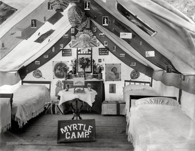 New Zealand circa 1905. "Sumner, Christchurch. Interior of large tent decorated with posters and picture postcards, with tallboy and mirror, trunks with flags, lamps and 'Myrtle Camp' sign." For the men of Myrtle Camp, all the comforts of home and then some. Glass plate by Adam Maclay. View full size.