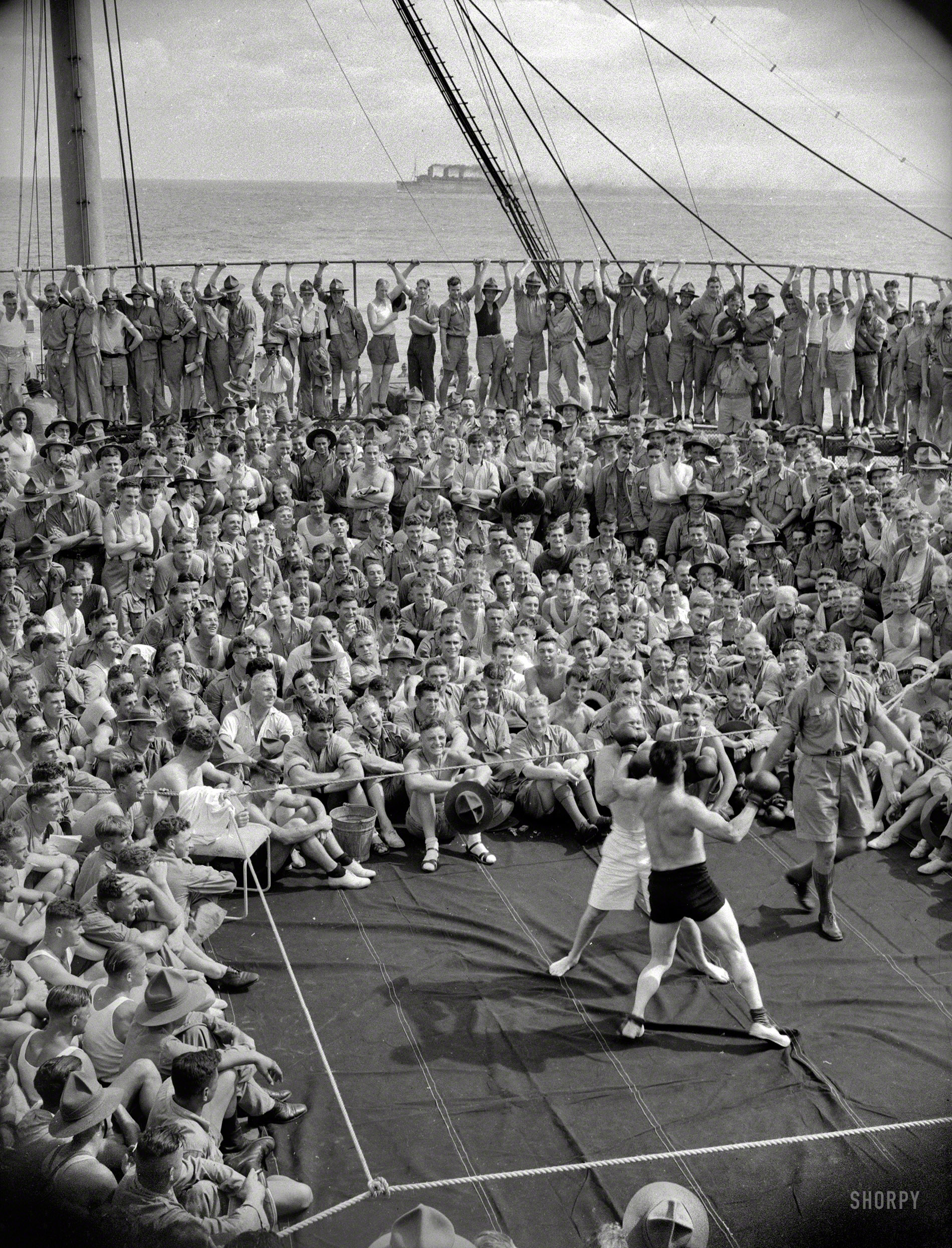 Circa 1940, somewhere on the high seas. "Boxing match in progress on the deck of New Zealand troopship Dominion Monarch, carrying 2nd Echelon 4th Reinforcements to the United Kingdom. Probably Empress of Russia seen sailing in the background." View full size.