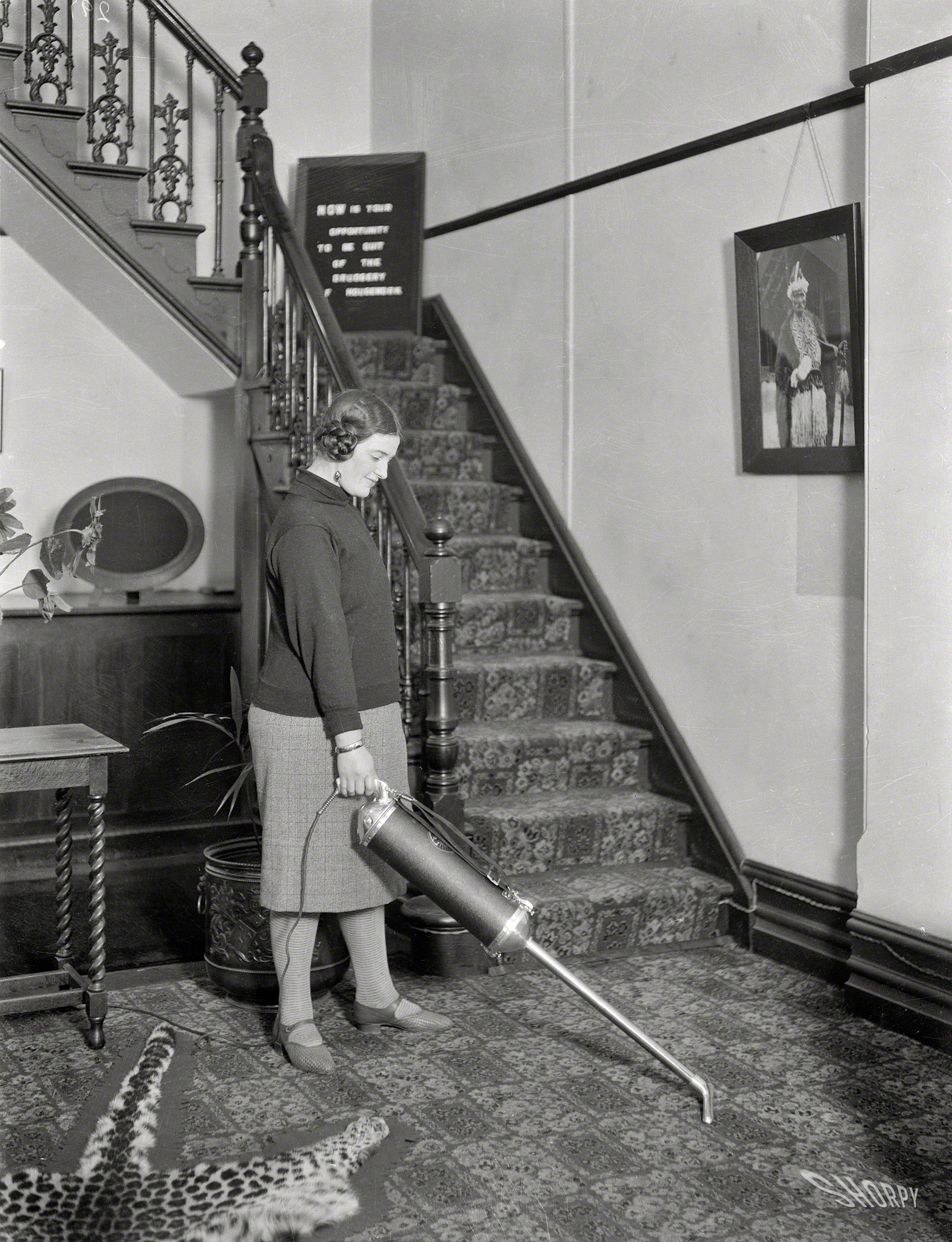 Wellington, New Zealand. "Woman using a vacuum cleaner in a hallway, photographed early 1930s by Gordon Burt." Sign on the landing: "NOW is the opportunity to be quit of the DRUDGERY of housework." View full size.