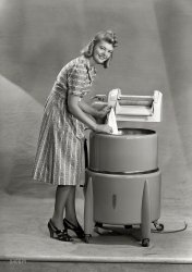 New Zealand circa 1950s. "Model with wringer washing machine." I am Woman, see me Wash. Photo by Gordon Burt Studio. View full size.
Something missing.There is no plug on the washing machine. Kind of hard to wash clothes without one. 
Something vital is missingShe will be able to get a lot more done if the washer was connected.   Why no plug, and just an unterminated cord?
Perhaps it is the precursor to inductive charging.
Lucky GirlMen in the Western civilization have always spoiled our women by allowing them to have electric appliances, educating them, and allowing them to carry their own money.
Me being picky I'm sure she'll get better performance out of the machine, when there's a plug on the end of the cord - and it's plugged into a socket.
[I guess no one noticed the title of this post. - Dave]
Yep, a point too subtle (for me) at that time of the morning.
New Zealand LaundryNew Zealanders must be quite eccentric to be able to wash clothes in an unplugged washing machine. Either that or they are much smarter than the rest of us to have figured out how to get the machine to work without plugging it in.
Princess IndeedIt blows my mind to think of doing laundry (even with today's machines!) in a dress, stockings and heels. Oh and with my hair curled.
[Princess is, for those who have not zoomed in, the brand of the machine. - Dave]
A Bit Ahead of its TimeMust have been invented before wall outlets and plugs on cords.  But at least it's not gasoline-powered like the one my grandmother had.  As a kid of six, I spent a summer with her and laundry day was a noisy outdoor affair with the old one-banger.  Primitive as it was, it was the once convenience Grandma had.  The whites got boiled over a wood fire in an old cauldron with "bluing".  This young woman looks like a twin for my niece, but thankfully my niece got a new washer and dryer just yesterday.
Somebody cut the plug offWhy?
One of the wheels is bentPoor machine must have had a hard life.
That&#039;s settledNow that the plug explanation has been crowd-sourced, what color would that magnificent contraption be?  It predates the fad for avocado or harvest gold appliances, but even in grey scale, it's pretty clear that the tub is not "refrigerator white."
Three wireObviously she won't get much washing done with the cord hanging loose like that, but I see that at least she will be protected from electrocution once they get the thing properly wired up.
That washer won&#039;t wash.Is there some sort of world wide conspiracy to sell washers without a $#@% electrical plug attached to the power cable?
Pretty model.
This will work much betterIf you have the power cord end attached.
Plug: optionalMost likely, this appliance was sold in several countries, necessitating plug installation at points of delivery to be compatible with the outlets used in that locale.
Danger: Electrocution hazard!Unplugged?!?  There's not even a plug on the end of the cord.  Her hairstyle could undergo a radical transformation when she pushes those wires into the wall socket.
Kiwi KitchenThe high end kitchen appliance manufacturers Fisher and Paykel is a New Zealand based company. They developed the "kitchen drawer" dishwasher.
TeslaIt worked on the Tesla principle he invented where electricity was broadcast through the air.
Safety firstNo plug on the cord insured that the that pretty lady didn't get any part of her pretty self caught in the wringer.
No plug ?In some countries,like the UK, there was no one standard electrical outlet as in North America. Appliances were supplied with no plug, so that the user could supply the one that fit their particular outlets.
Customer SuppliedVarious options exist for the connection of electrical equipment, especially in earlier days or across different regions.  Existing outlets of different ratings will have different plug configurations.  Direct hard wiring of larger appliances is sometimes used with a disconnect switch that is surface mounted on the wall.  The customer or installer would buy and attach the appropriate cord cap to match a particular location or existing outlets.
Brings Back MemoriesI remember clearly at the tender age of 4 helping my grandmother with the laundry and getting my arm caught in the wringer.  Fortunately, she wasn't too far away and released it before any damage was done.  But even to this day my right arm seems a bit flat.
Standards are great, there are so many to choose fromIt's just barely possible that sockets and plugs weren't as standardized in 1950s New Zealand as they are today.  It may have made sense to ship appliances with no plug, and let the dealer or customer install the right plug to match the customer's house.
An example from another country: The UK officially switched to their current plugs and sockets right after WWII, but the previous standards remained in use.  For a while it was *illegal* to sell an appliance wthere ith a plug on the cord - the theory was that if somebody bought an appliance with the wrong plug for their socket, they would just chop the plug off, leaving a plug with a bit of wire sticking out the end.  A small child would then find this plug+wire, somehow find a matching socket, plug in the plug+wire, and zap themselves.  In theory, anyway.  Part of the regular school curriculum was "how to wire a plug".
Plugs might not have been standardizedI seem to recall on an electrician's forum several years ago, that one Australian had dug up some documents showing that their standard plug only dated to 1938 (and it is well-documented to be originally an American design). Australia and New Zealand now share the same electrical standards, but I don't know if this was true in the '50s. Even today, I think many appliances in the UK require the user to install their own plug (witness the Tenth Doctor Who describing Donna Noble as someone who "can't even change a plug").
A benefit of waiting so late is that the need for grounding appliances was already evident. I have a 1930 American book warning of the special hazard of not grounding washing machines, and recommending using a plug that matches today's Australia/New Zealand plug. This advice was not officially sanctioned until 1947, and went mostly unheeded until 1962.
Mom&#039;s warningI can still remember my mother telling me in no uncertain terms not to put my fingers anywhere near the wringer and that was probably 62 years ago. 
Plugless PrincessLack of standardization of international electrical socket configurations and standards at the time led some manufacturers to ship their machines without plugs. It was the responsibility of the local installing dealer to provide a compatible one, be it with round pins, parallel or non-parallel flat blades, polarized or whatever. Also, jumpers in a junction box inside the machine often had to be changed to match local line voltages or 120 or 220 and frequencies of 25, 50 or 60 Hz. Not having a plug on the machine was an attempt to insure it would get properly setup by someone who knew what they were doing (although it didn't stop resourceful 10 year old boys from taking a lot of things for pre-installotion test drives).
Why botherWe owned one of these dang things when I was a kid, my mom didn't need a plug on hers either because it was easier to go to the laundromat!
Colour of the tubI remember seeing machines like this in the second-hand shops and the colour always seemed to be middle-of-the-range green. Not dark green or pale green but somewhere in the middle.
(The Gallery, Kitchens etc., New Zealand)