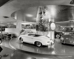 New York circa 1955. The Max Hoffman car showroom, with its motorized turntable, at 430 Park Avenue and 56th Street. Designed by Frank Lloyd Wright and recently demolished. Photo by Ezra Stoller. View full size.
Rolling InvestmentsThe four beauties sitting on that wonderful turntable are probably worth in the neighborhood of $400,000 today. Nice neighborhood.
Outer PorscheErwin Komenda, a Porsche employee, is generally credited with designing the early 356 exteriors, while the mechanicals were essentially VW. The pictured coupe is a 356A 1500, and the ragtop a 356 Speedster. The Speedster came to be (late 1954) as a result of Hoffman persuading Porsche brass that a "low cost" convertible would sell well in the American market. Just a few blocks west of Hoffman's store, Luigi Chinetti was selling imported Ferraris on West 55th Street.
Import ManiaMax Hoffman started the whole import craze. He was the first to import most of the European marques including Volkswagen and all of the British cars. He brought in the first Japanese cars (Toyota) as well. Eventually they all became independent from his company, but he laid the groundwork. 
Another unique space lost.This was a rare Wright interior that should have been saved.
[Seriously? It's private property, a commercial space that was there for almost 50 years and suited only for displaying cars. - Dave]
Dave - Granted saving interior spaces is rare and difficult, I merely suggest that this one was worthy of at least consideration by the owner. And who's to say it wouldn't be suited for something else? It could have been the most unique TD Bank in the city (lord knows there's enough of them). They could at least have given people a chance to see the space, document it, etc, before demolition. 
The Rest of the StoryGreat NYT article on Max Hoffman.
Moved To JaguarI remember visiting this showroom after I got hired by IBM across the street at 425 Park Avenue in 1967. At that time,the showroom was full of Jaguars although not sure if being sold by the same owner.  Here I was, at 18 years old, making $105 a week and looking at brand new XKE's.  At least it didn't cost anything to look.
HoffmanWas also, I believe, able to convince Mercedes-Benz that he could find a market for their 'Gullwing' 300SL coupe in 1955 for about $9,995 a copy! It was the Lamborghini of its day! Sold from '55 to '57, they only made about 1900 or so. It's still an exciting car to own and drive. 
(Cars, Trucks, Buses, NYC)