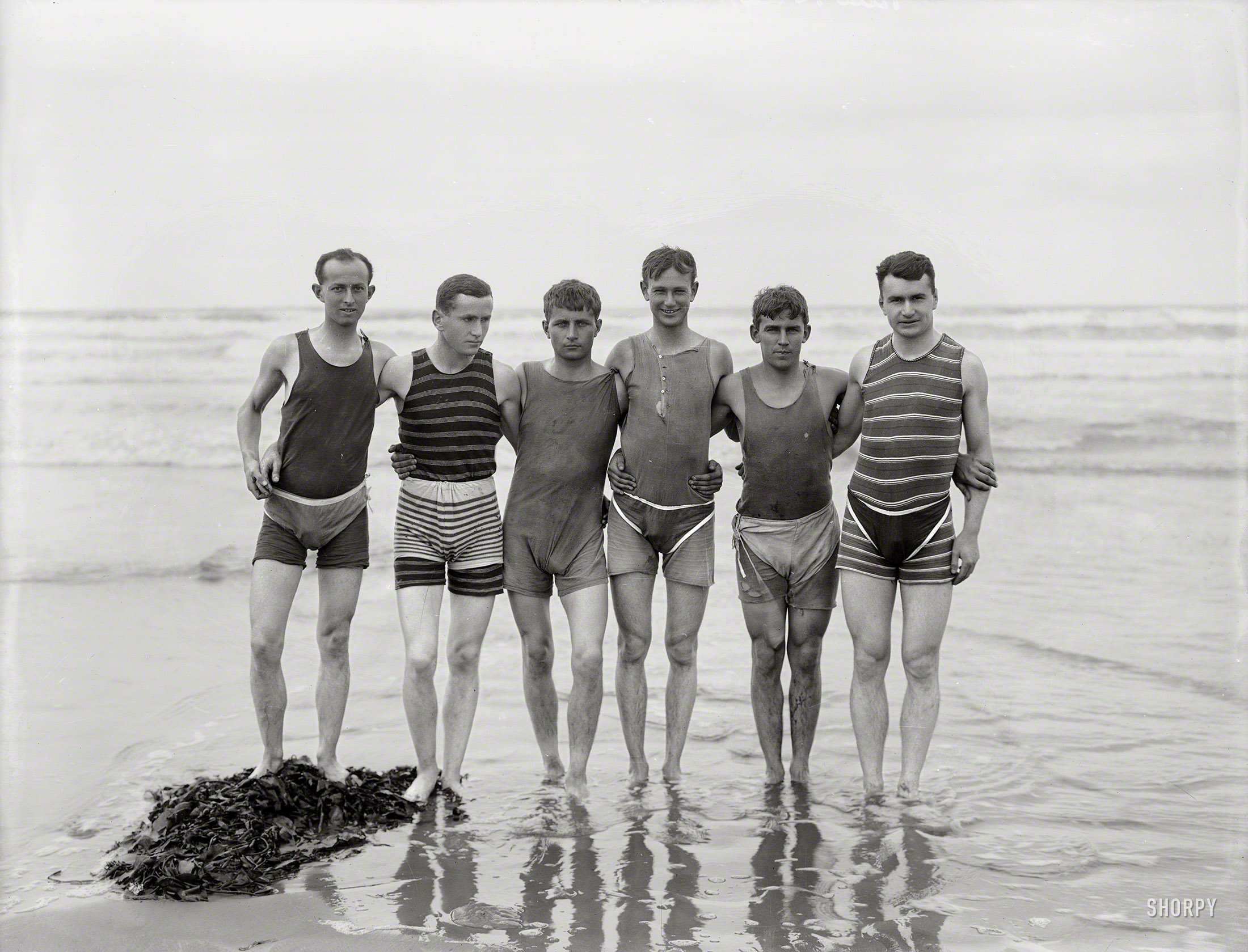 By 1910, men's bathing costumes were sleeveless and cut off at mid-thigh. However, as required by some bylaws, many male bathers, such as this group, wore trunks over their one-piece suits.
-- Encyclopedia of New Zealand
New Zealand circa 1910. "Unidentified bathers, probably at Christchurch." Dry plate glass negative by Steffano Francis Webb. View full size.