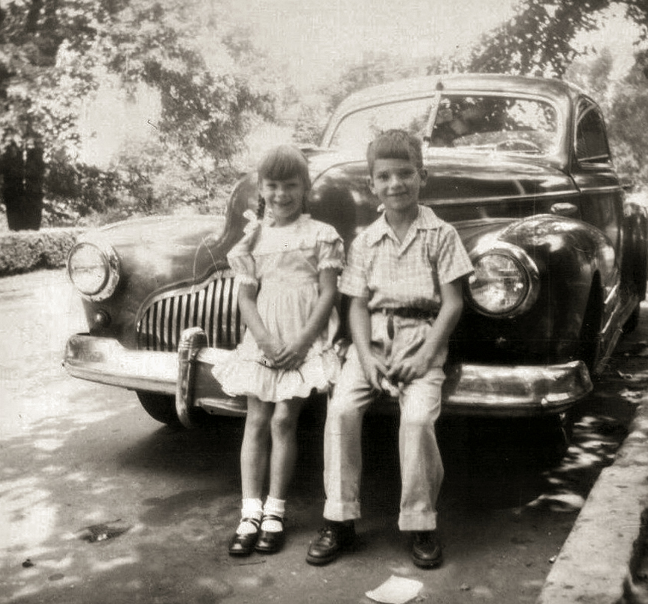 My sister and brother in a 1949 photo, on Second Avenue in Altoona, Pennsylvania. Not many years later, at 16, I demolished this Buick (and please take notes if you'd like to demolish a Buick) skidding on wet streetcar tracks -- too much speed might have been involved -- and nailing a brick porch next door to Sacred Heart Convent on Sixth Avenue. A woman appeared (the Madonna?), shouting "You've wrecked!" and because a few more bricks were thudding onto the hood, I said, "I believe I'm still wrecking." View full size.