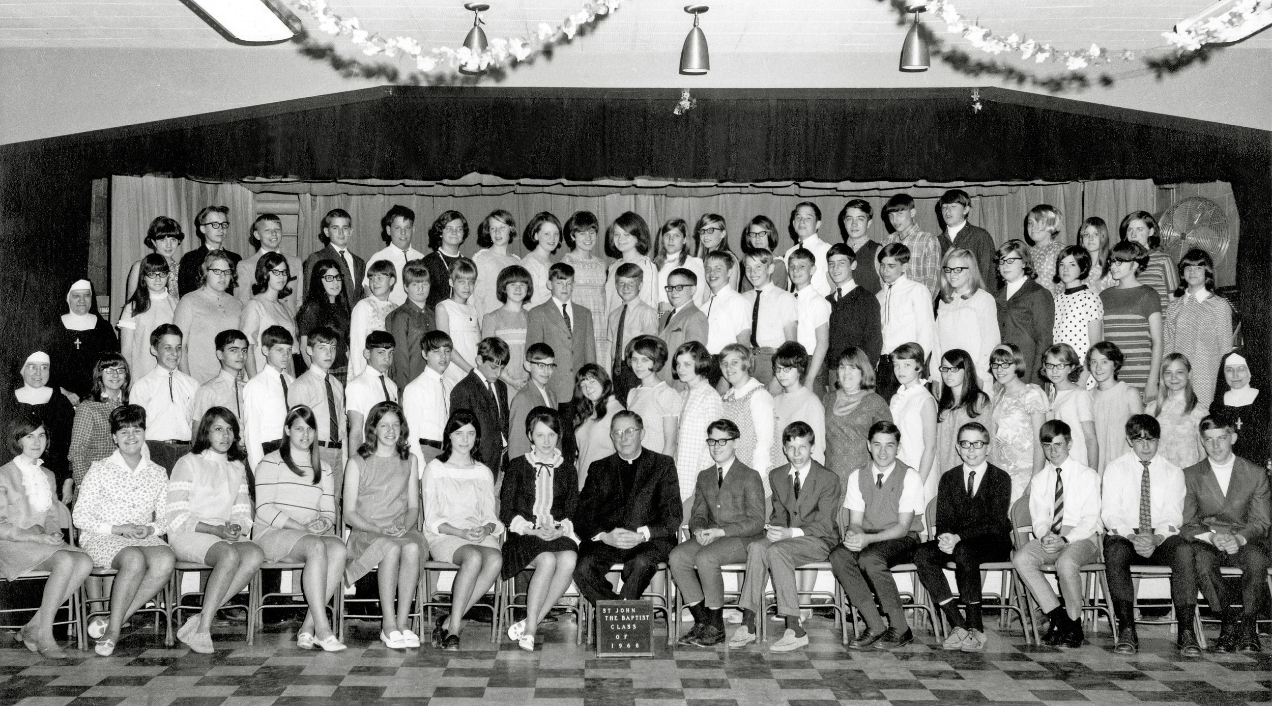 This is the graduation picture for the 8th grade class at St. John the Baptist Catholic School in New Brighton, Minnesota (a suburb of St Paul). I'm in the second row from the front, fourth from the left. 

This was one of the few days each year when we weren't required to wear our uniforms (but I inexplicably still wore the stupid string tie!)

Reverend Paul Koscielniak, who ran the school from its inception in 1952, is front and center.

My biggest surprise, when scanning this image, was seeing what appears to be mistletoe hanging above center stage. Wish I had seen and taken advantage of it back then! View full size.