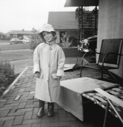 My mother did not allow “wasting film” on pictures of cars. Film was meant to be wasted on pictures of clothes. So, when she bought me my first raincoat for the spring of 1959, she had me dress up in my boots and that yellow slicker, and pose on the porch that my father had added to the front of our first home in Levittown, Pennsylvania.
As a picture of a smirking kid in a too-big raincoat, so the sleeves have to be folded up, it is kind of lame. But it is one of only two pictures of our 1952 Studebaker Commander, which is the car sticking out of the carport behind me. That car meant the world to me because in deepest, darkest suburbia, nothing ever happened unless you got in the car. It took you to the drive-in movie, and Dairy Delite ice cream. Home was boring. Cars were exciting.
(ShorpyBlog, Member Gallery)