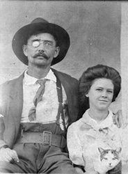 My grandfather Benjamin Franklin Taylor and his daughter Camilla and cat.  The photo was taken in Marked Tree, Arkansas in 1909.  Ben had lost his right eye in a hunting accident on the St. Francis River when he was younger.  In this photo he is wearing a gun belt and is carrying a Navy Colt.  Marked Tree was a dangerous logging town and men wore guns for protection.  A year after this photo was taken Camilla, my grandmother, would at the age of 15 marry Wm Robinson, age 31. View full size.
(ShorpyBlog, Member Gallery)