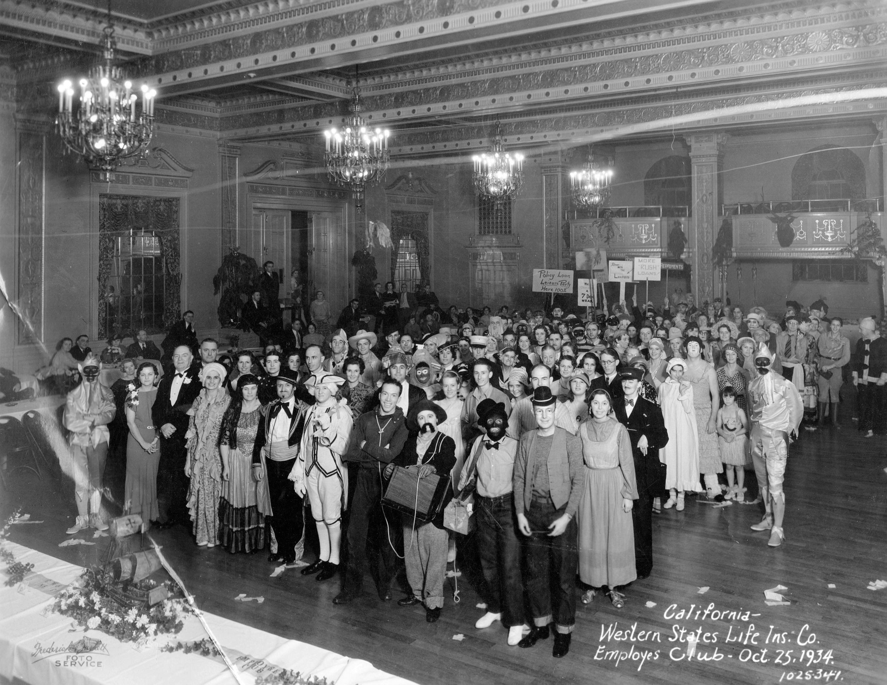 Costume party for the Western States Life Insurance Company Employees' Club, Oct. 25, 1934. I think this was taken in the Grand Ballroom of the Masonic Temple in Sacramento at 1123 J Street, which still exists. One of the employees was my wife's aunt, who I believe is three rows back on the right and hidden by the conductor; her friend Marion is in front and to the right of her. View full size.  