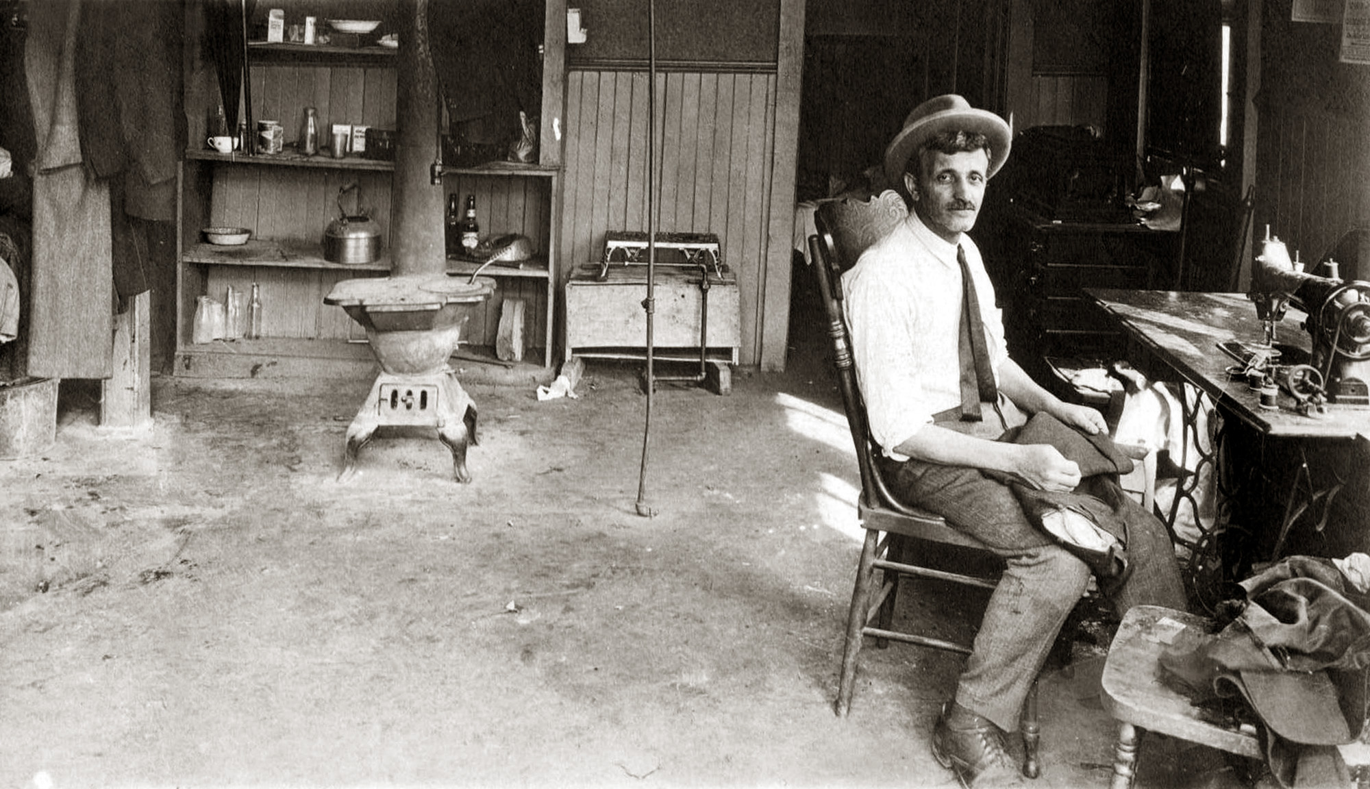 Photo was taken in 1929 in Wolf's tailor shop and apartment in Erie, Pennsylvania. He lived in the back of his shop - you can see his meager cooking  utensils and a Victrola on the dresser behind him. His family was in Brooklyn, New York. More here.
 View full size.