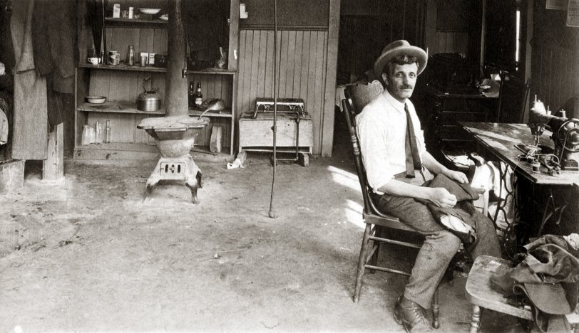 Photo was taken in 1929 in Wolf's tailor shop and apartment in Erie, Pennsylvania. He lived in the back of his shop - you can see his meager cooking  utensils and a Victrola on the dresser behind him. His family was in Brooklyn, New York. More here.
 View full size.
