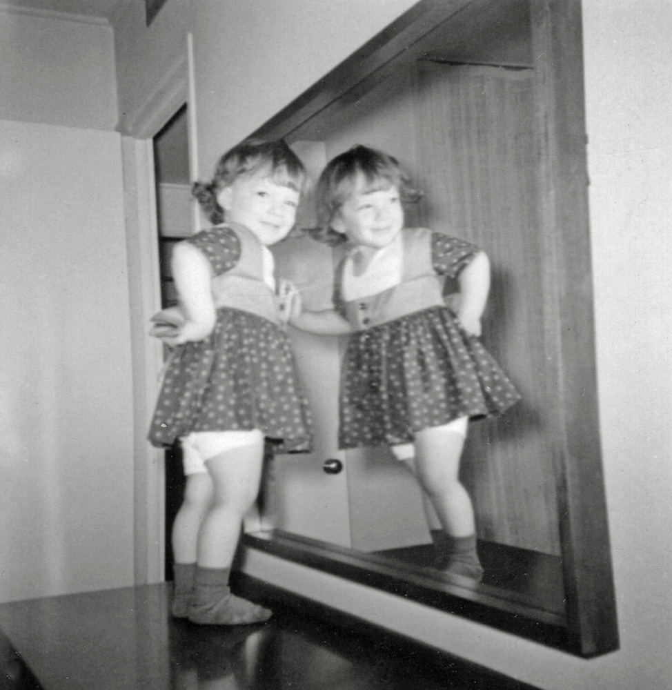 One of my favorite toddler games was playing that the mirror across from my mother’s bed was a television screen. Usually I would jump on the bed and watch myself “on TV” jumping. In this case I seem to be standing on her dresser in my socks without my shoes. But the game is the same, watch yourself on this pretend television set.