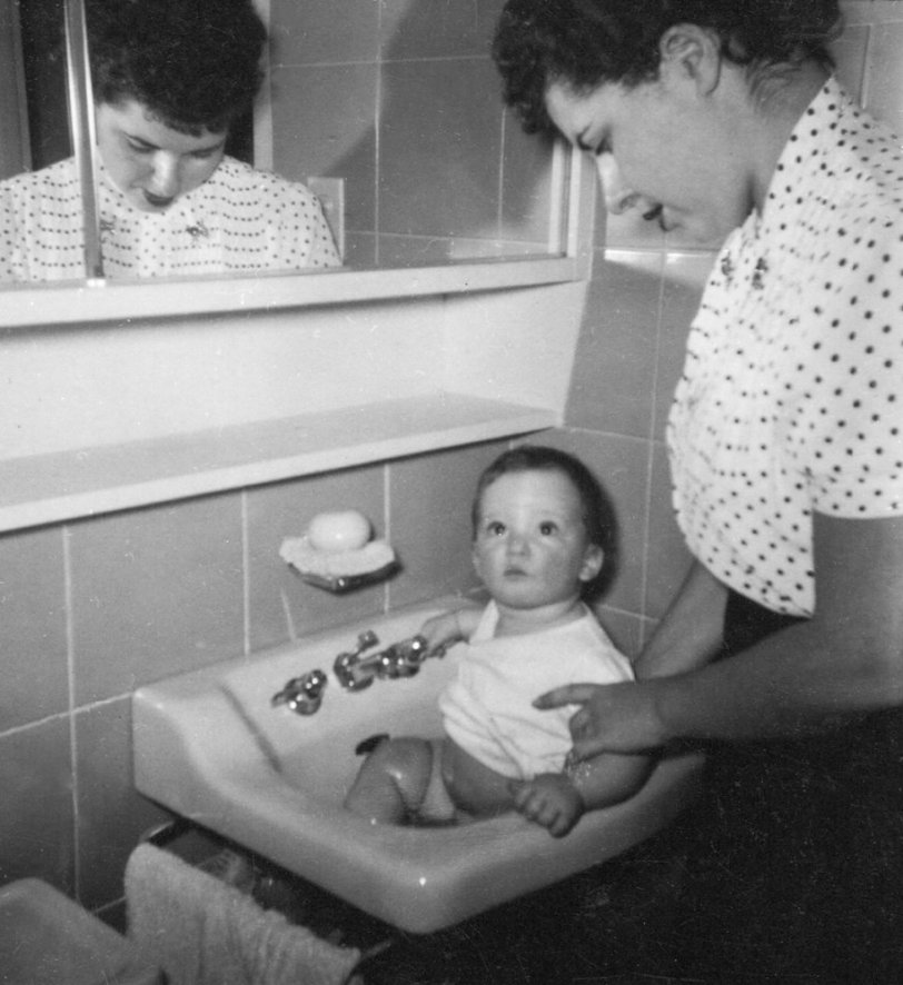 The Levittowner homes in Pennsylvania only had one bathroom. It had gray nine inch metal wall tiles and ivory fixtures. As a baby I was often set in the bathroom sink to have my face washed for bed. In this picture, snapped by my father (who I am looking at) she seems to be washing my southern half, rather than my face.
